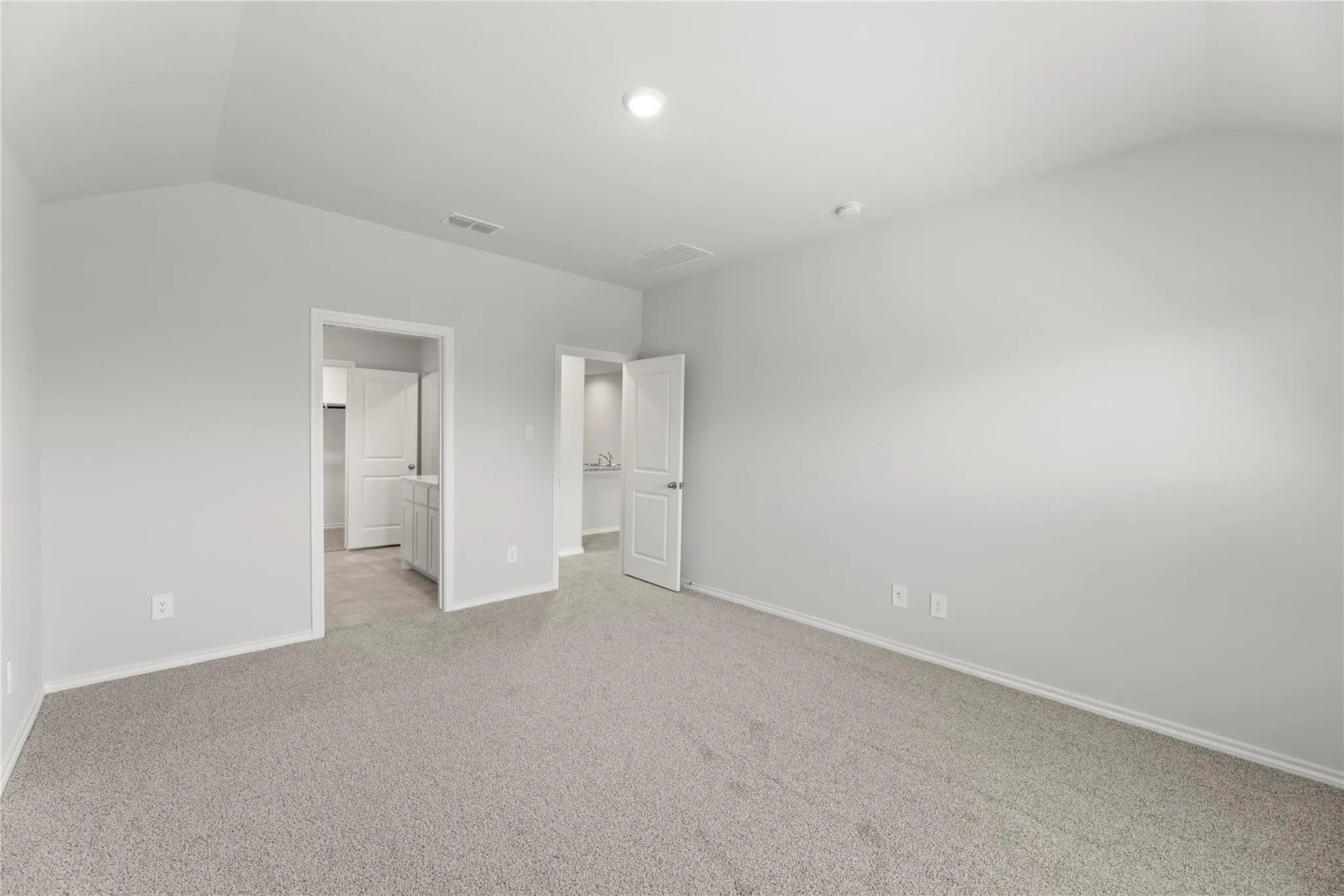 Spacious carpeted room featuring vaulted ceilings, light gray wall paint, and two entryways