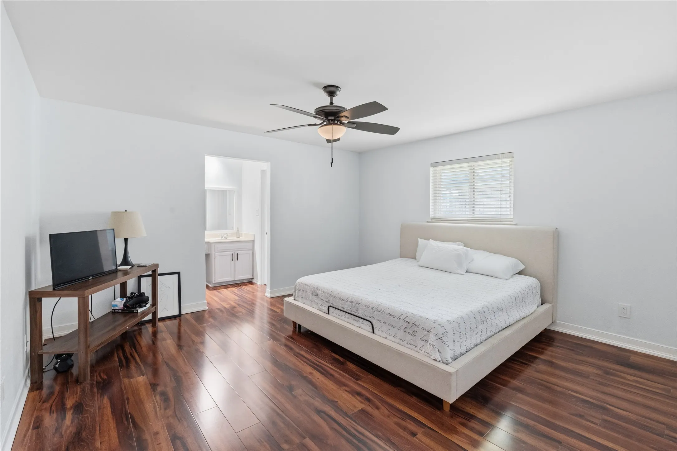 Spacious room featuring wood-finish flooring, a ceiling fan with integrated lighting, and white walls