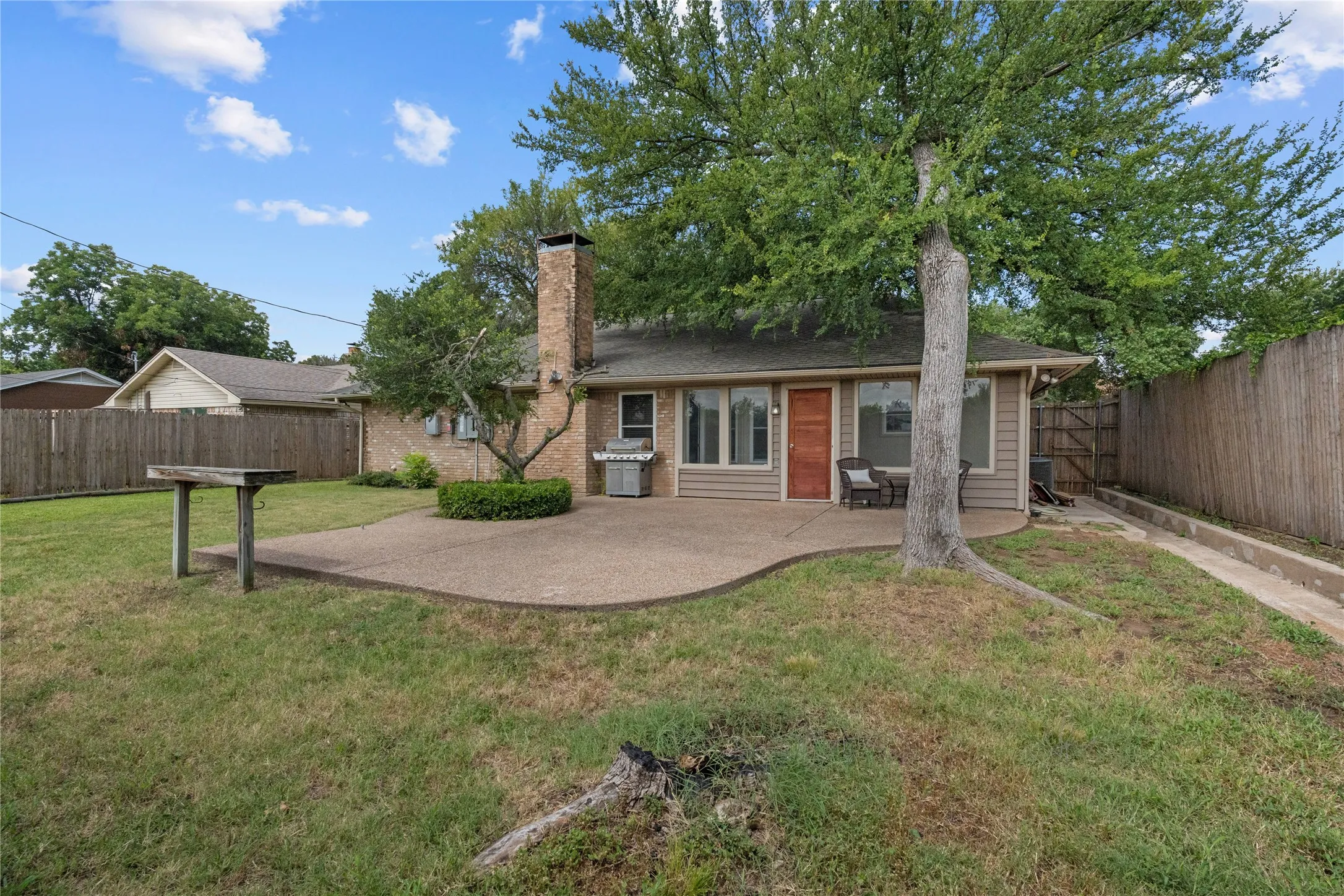 Expansive backyard featuring a large concrete patio, mature trees, and a wooden privacy fence