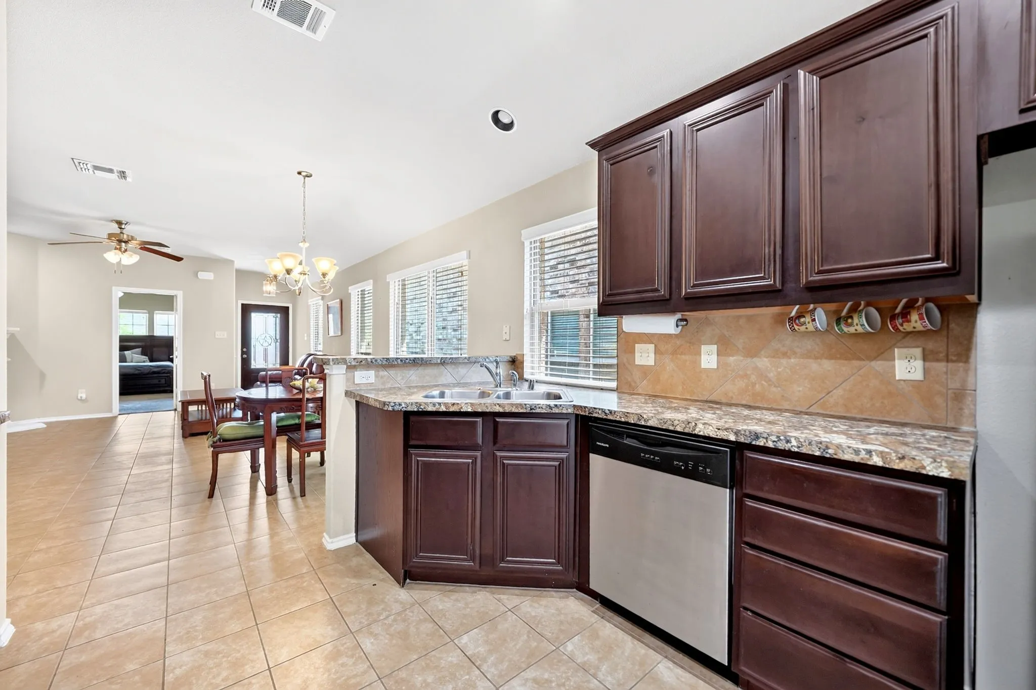 Kitchen featuring dark wood cabinetry, stainless steel dishwasher, double basin sink, and granite-style countertops