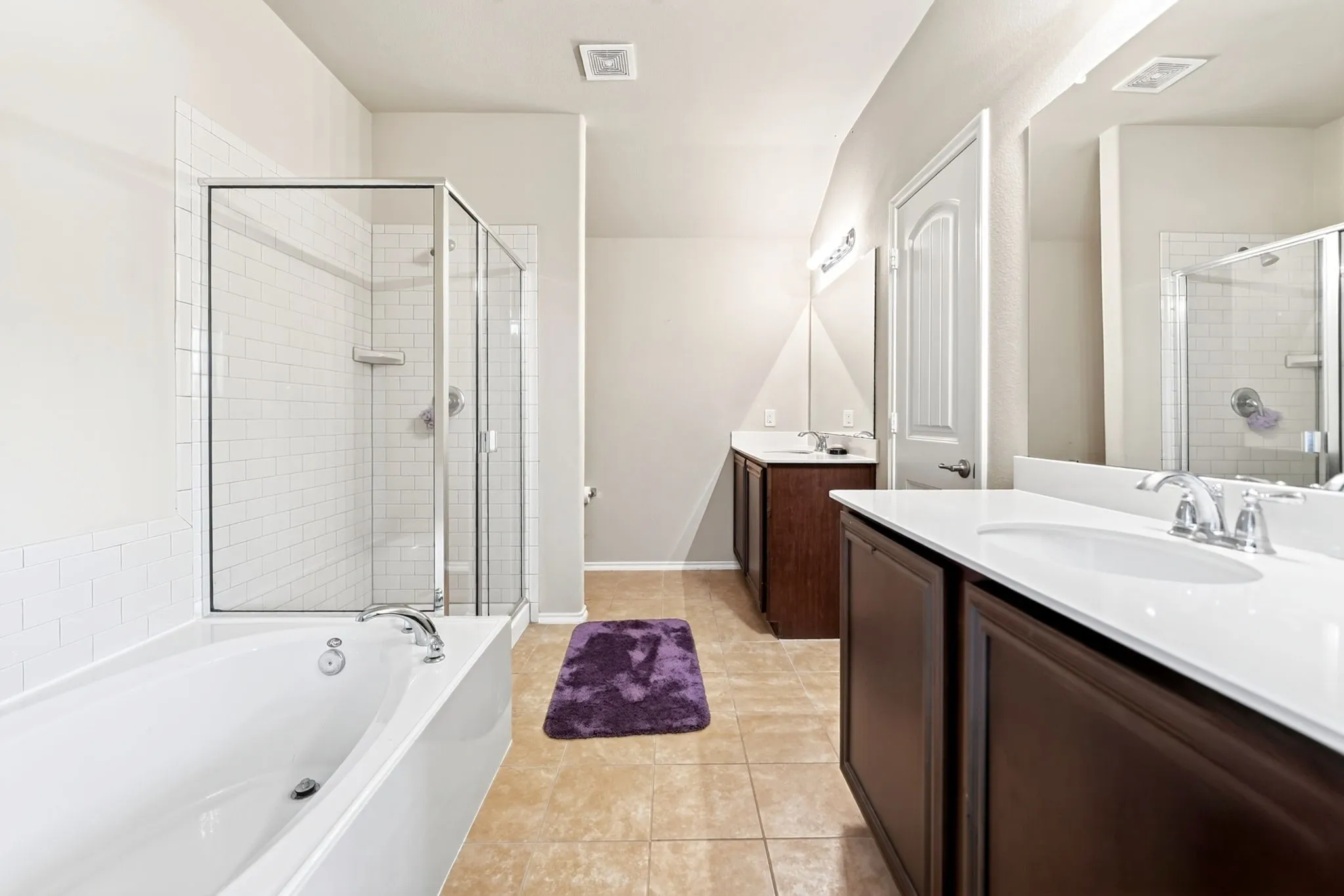 Bathroom featuring a white soaking tub, separate glass-enclosed shower with subway tile surround, dual dark wood vanities with white countertops, and tile flooring
