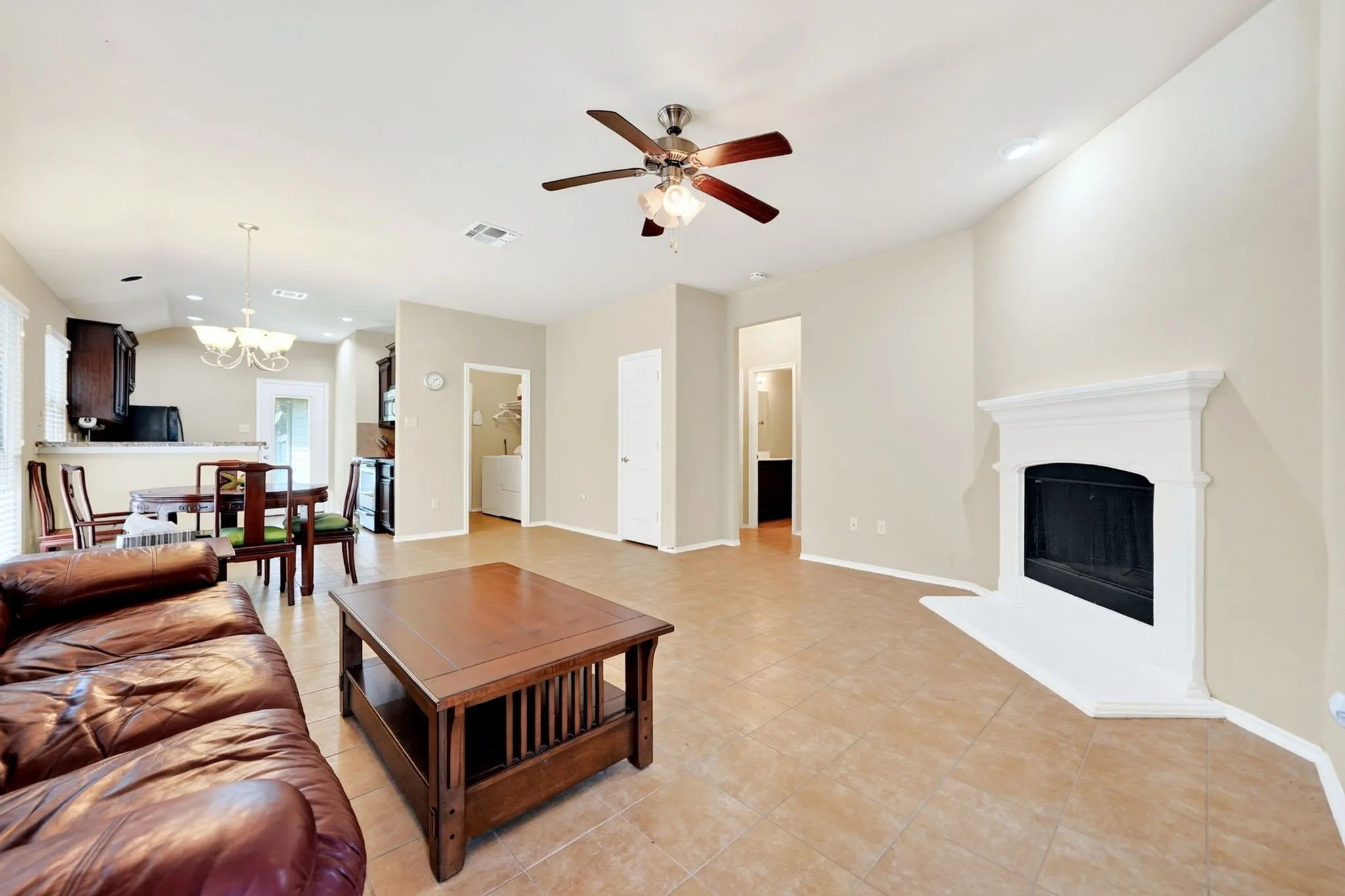 Living area featuring tile flooring, a white-mantled fireplace, and a ceiling fan with integrated lighting