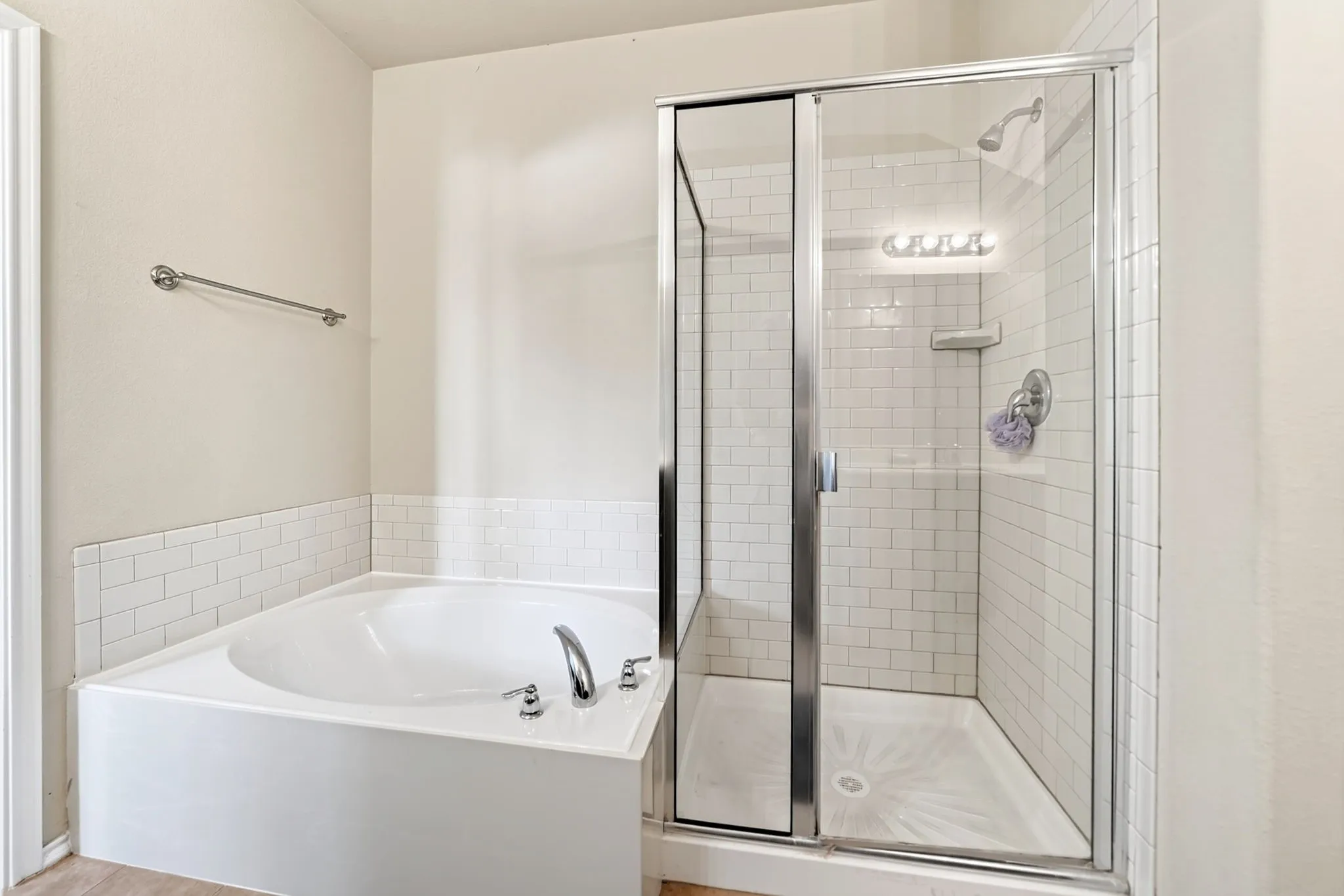 Bathroom featuring a white drop-in bathtub with subway tile surround, a glass-enclosed shower with subway tile walls, a chrome showerhead, and a chrome faucet set