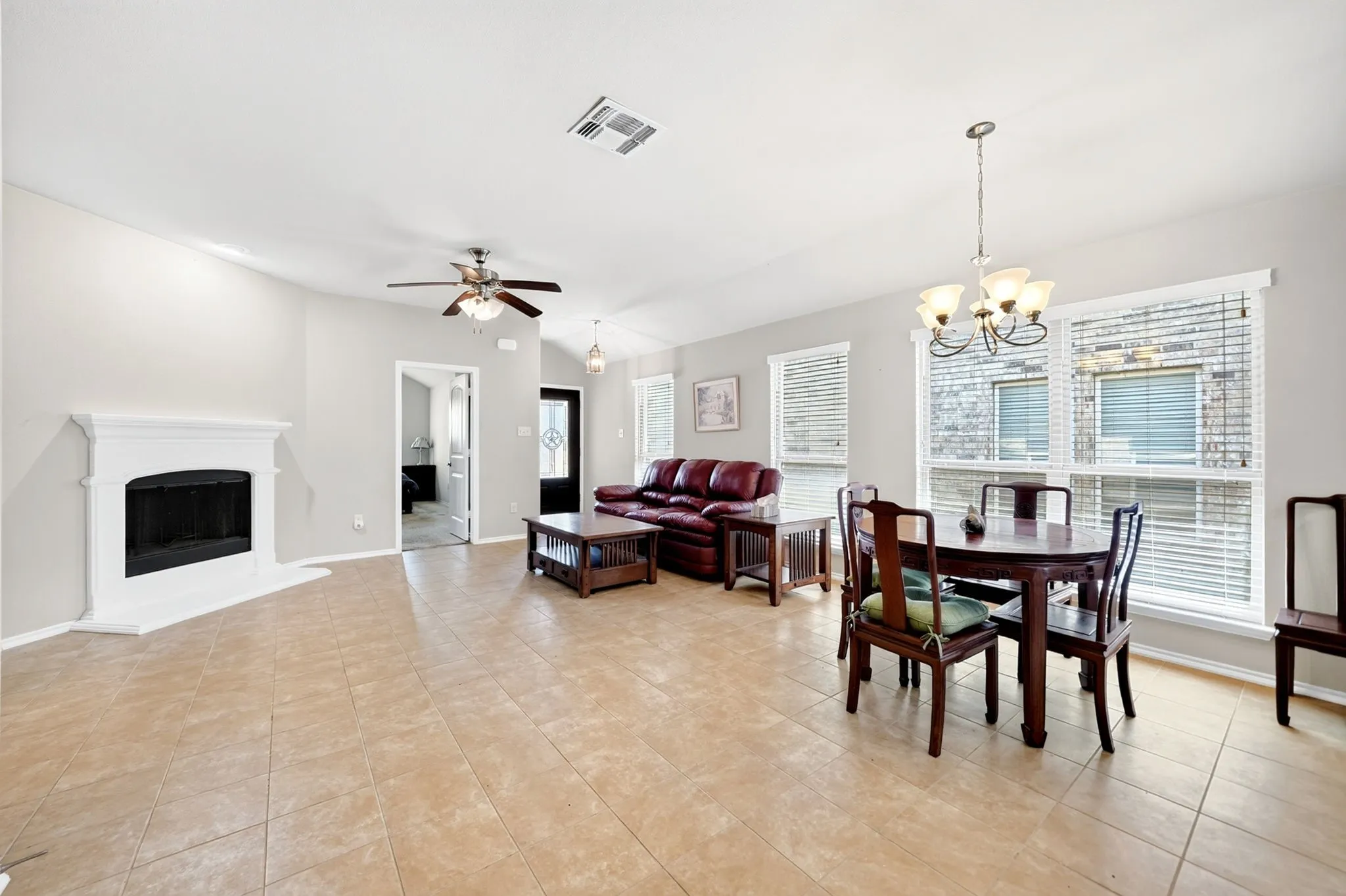 Open concept living and dining area featuring a fireplace with a white mantel, tile flooring, and vaulted ceilings