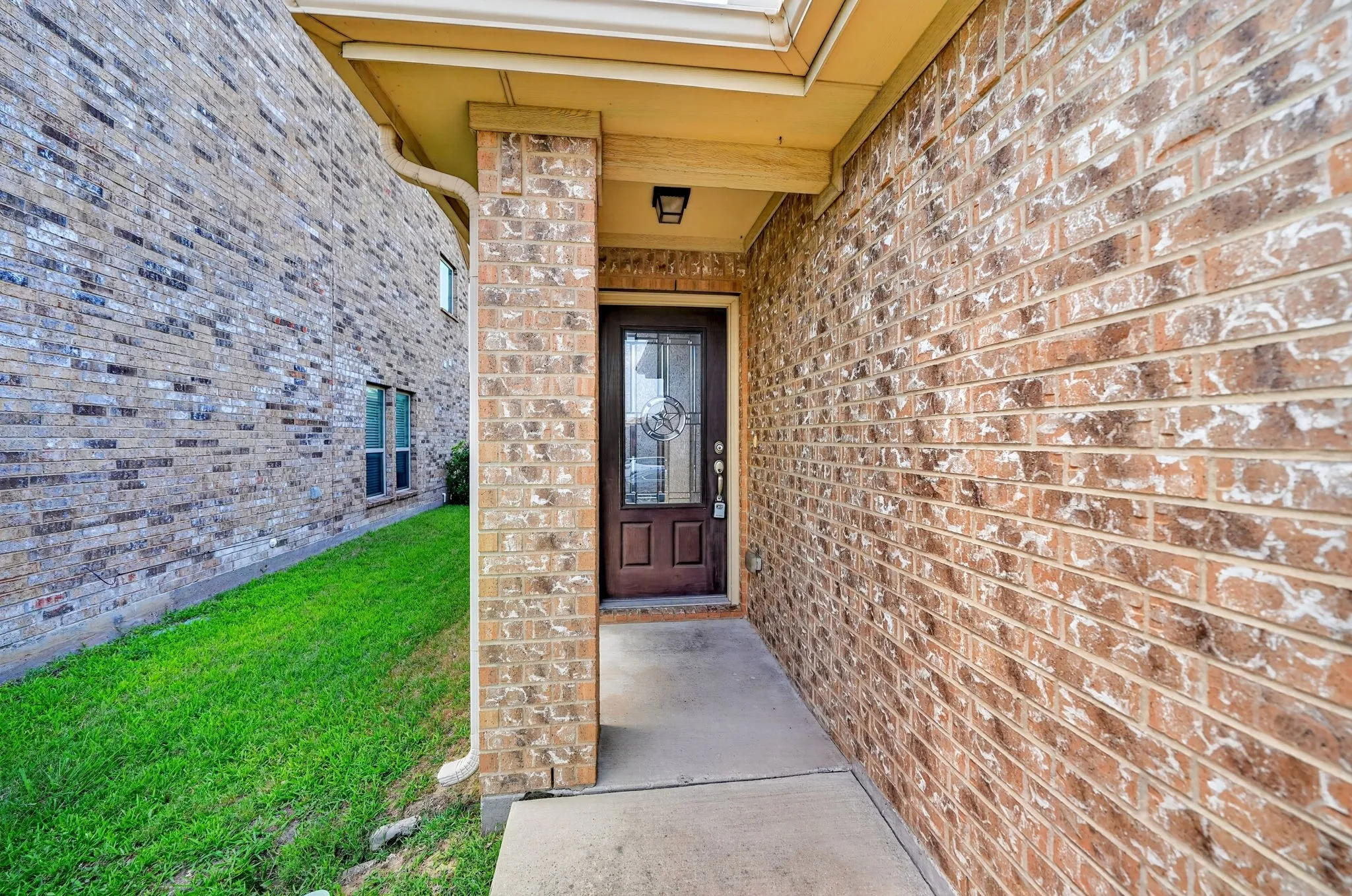 Brick exterior featuring a covered entry, dark wood-finish door with decorative glass inserts, and a concrete pathway
