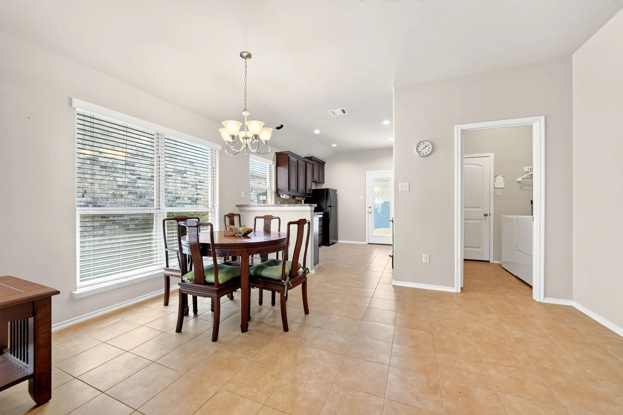 Open-concept living space featuring ceramic tile flooring, a large window with blinds, and a kitchen with dark cabinetry and black appliances