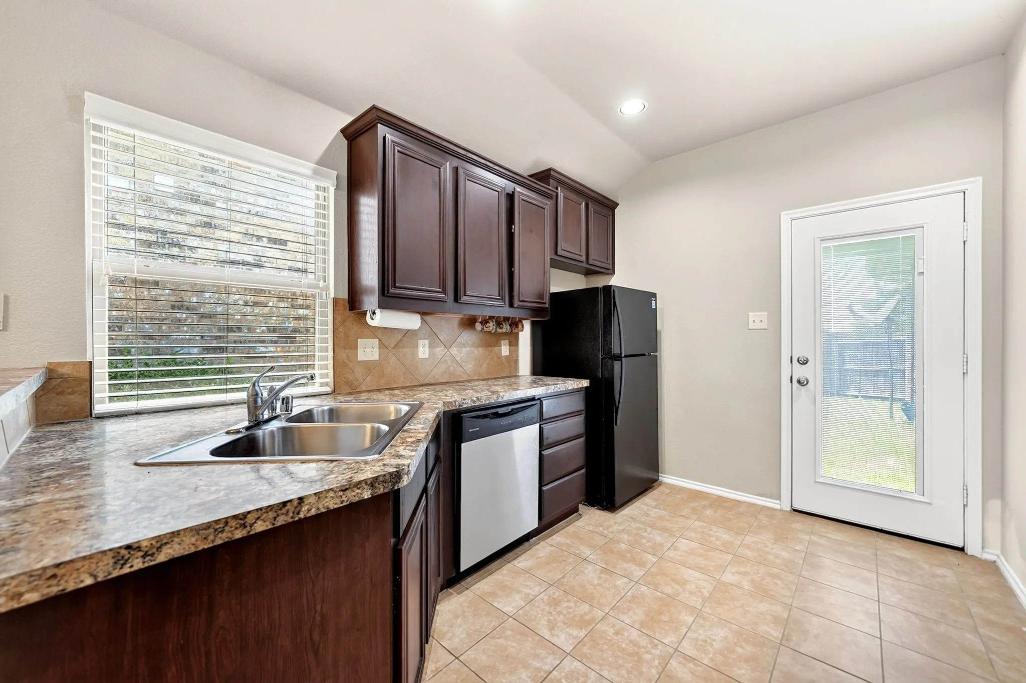 Kitchen featuring dark wood cabinetry, granite-look countertops, stainless steel double basin sink, and tile flooring