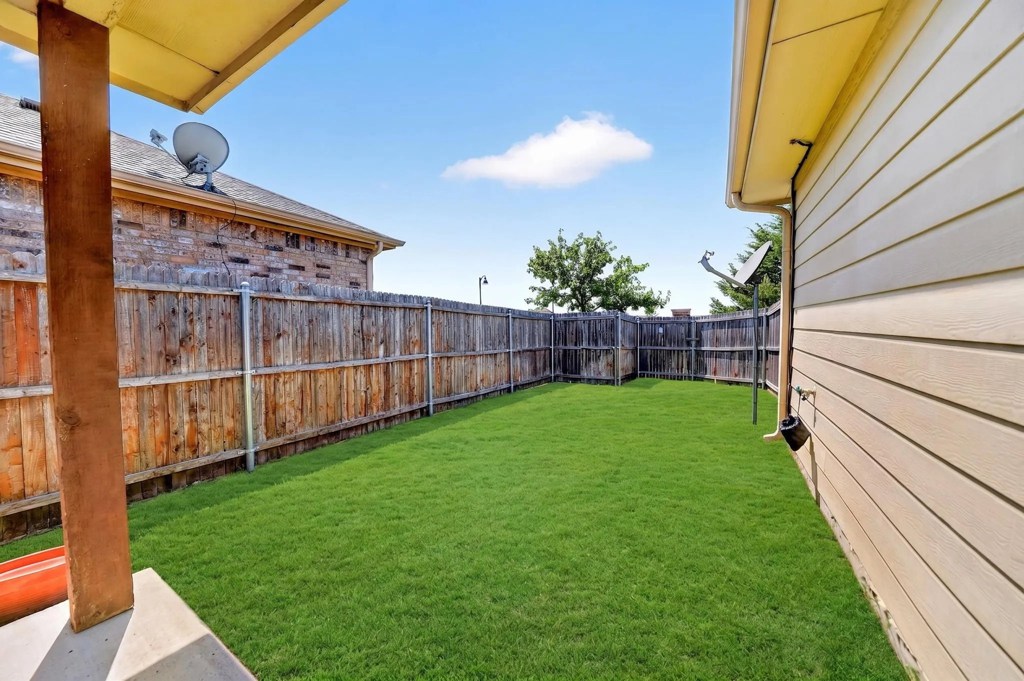 Spacious backyard featuring a lush lawn, privacy fencing, and a covered patio area