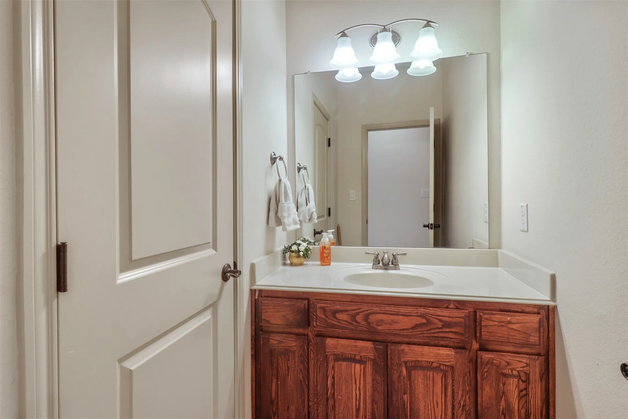 Bathroom vanity featuring a wood-finish cabinet, white countertop, and a single basin sink with a chrome faucet