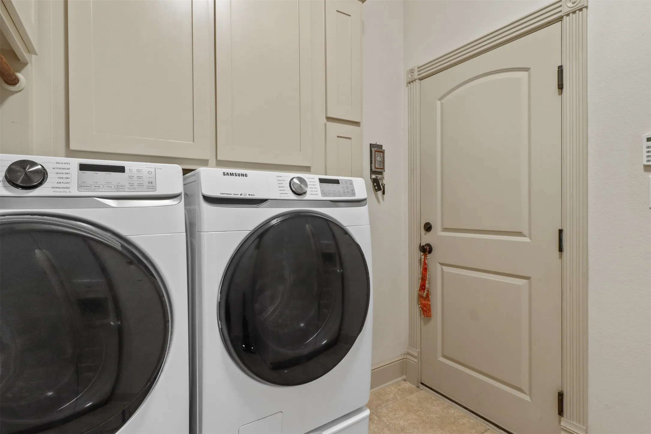 Functional utility space featuring light-toned cabinetry, tile flooring, and a paneled door with decorative trim molding