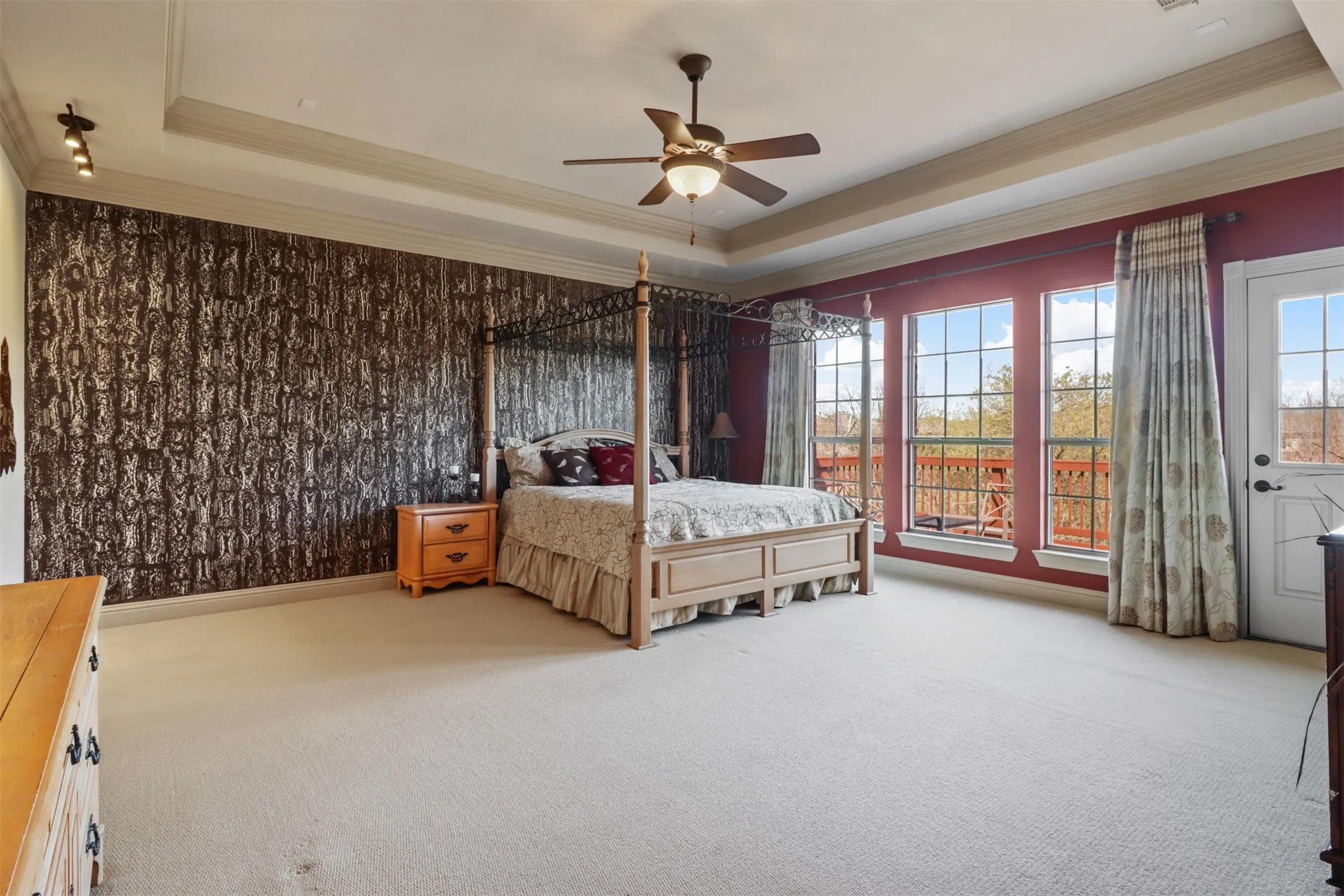 Spacious room featuring tray ceilings, a ceiling fan with light fixture, carpeted flooring, and a patterned accent wall