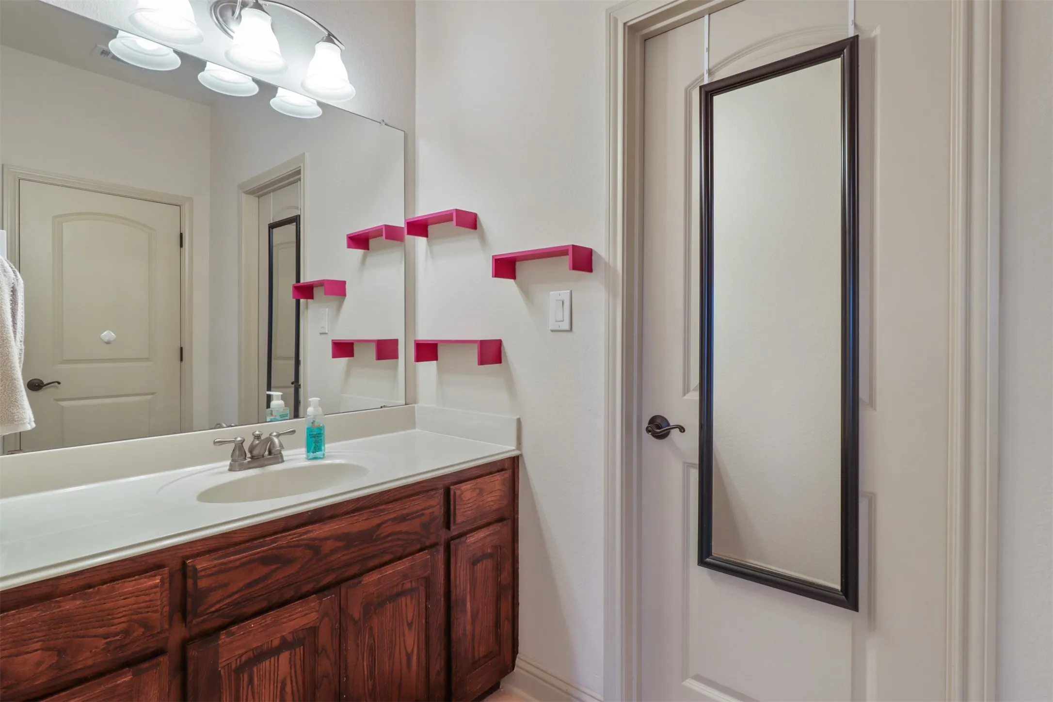 Bathroom vanity featuring wood-finish cabinetry, a white countertop, and a single basin sink with a chrome faucet