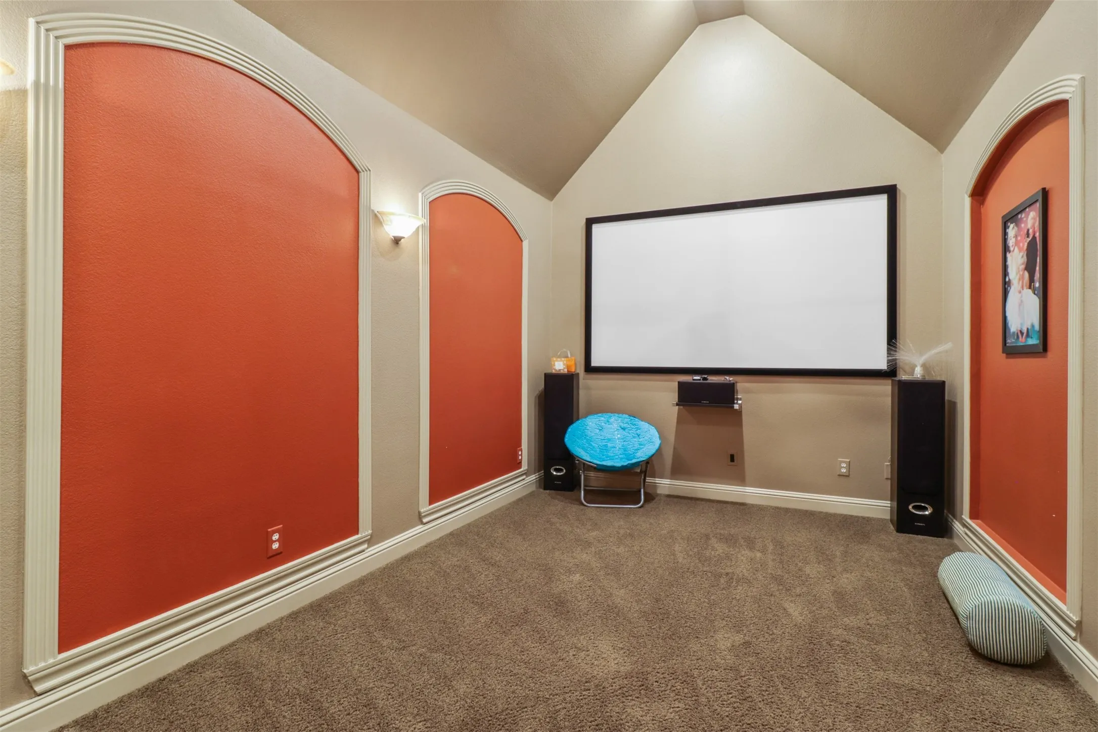 Vaulted ceiling room featuring a large projection screen, beige walls, and brown carpeting