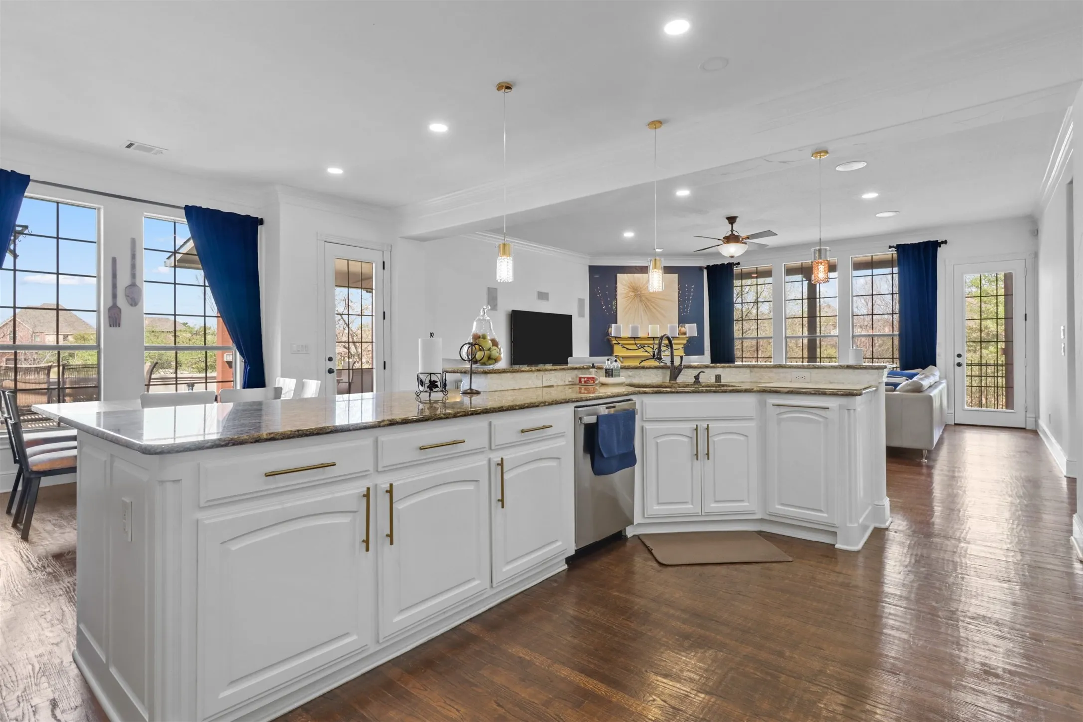 Spacious kitchen featuring a large central island with a granite countertop, white cabinetry with gold-tone hardware, wood-finish flooring, and ample recessed lighting