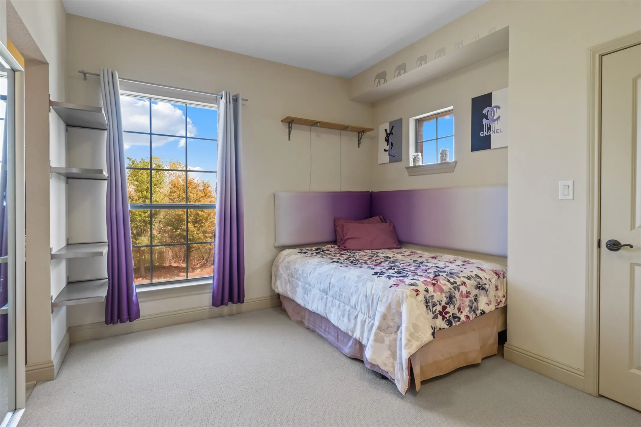 Carpeted bedroom featuring a large grid-pane window, built-in shelving, crown molding, and a solid interior door with dark hardware