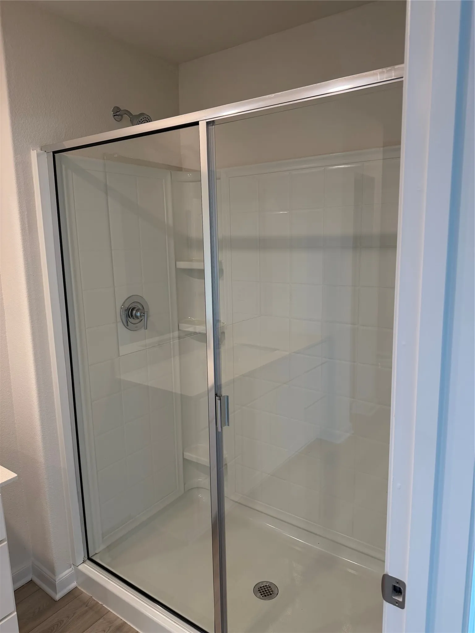 Glass-enclosed shower featuring white tile-patterned walls and an integrated bench