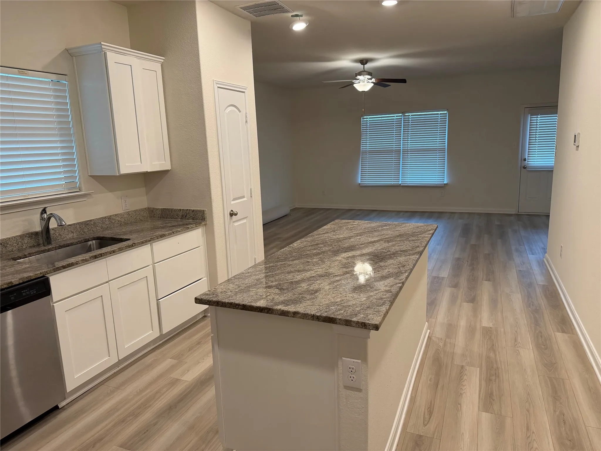 Kitchen featuring a granite countertop island, stainless steel dishwasher, white shaker cabinetry, and wood-finish flooring