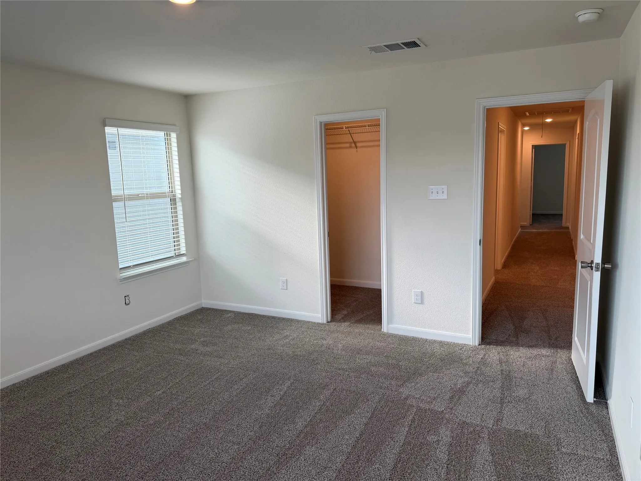 Spacious room featuring neutral carpeting, a large window with horizontal blinds, a white-painted interior door, a dedicated closet space, and recessed lighting