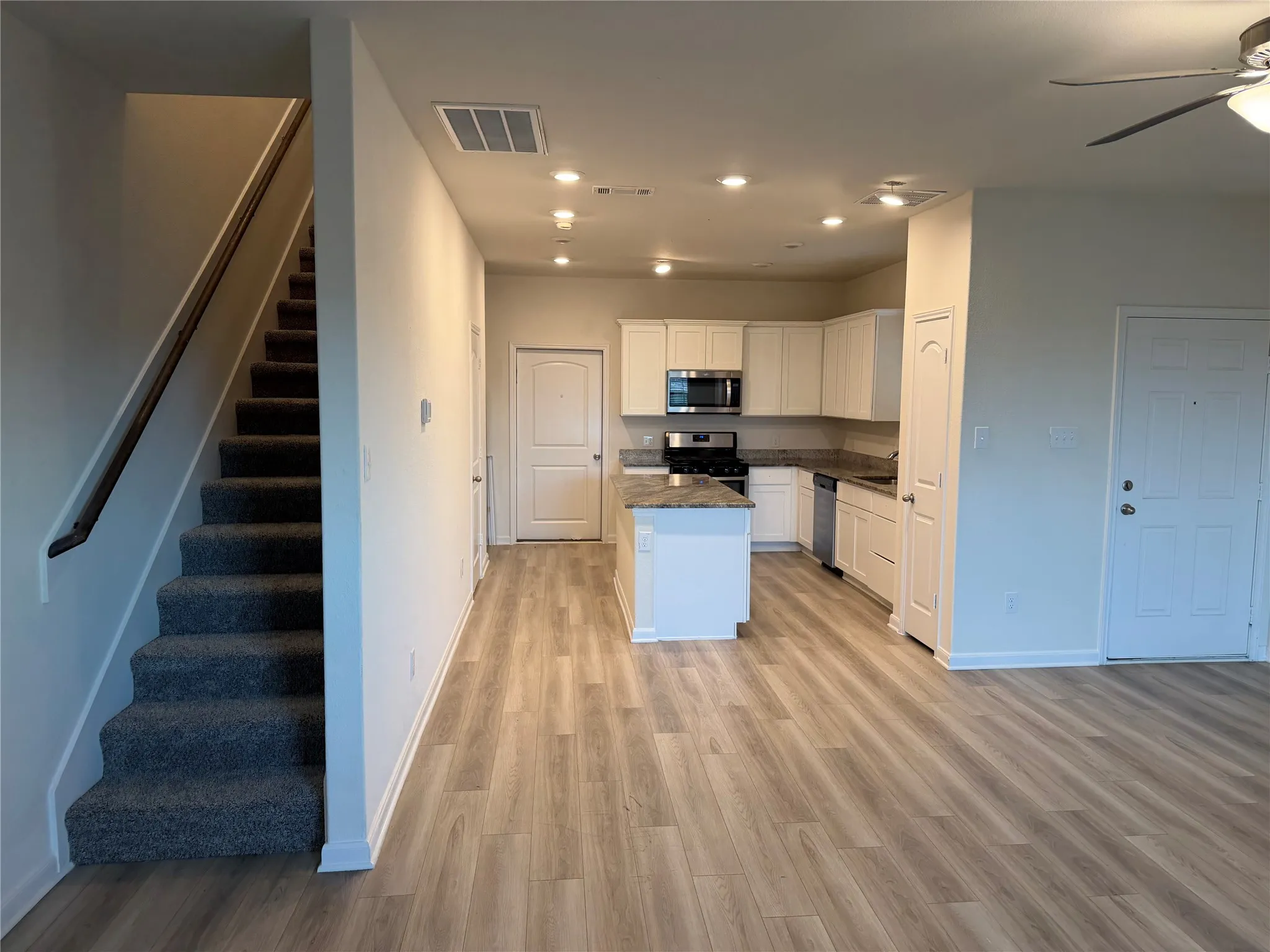Open-concept living space with wood-finish flooring, a contemporary kitchen, white cabinetry, a center island with countertop seating, and stainless steel appliances