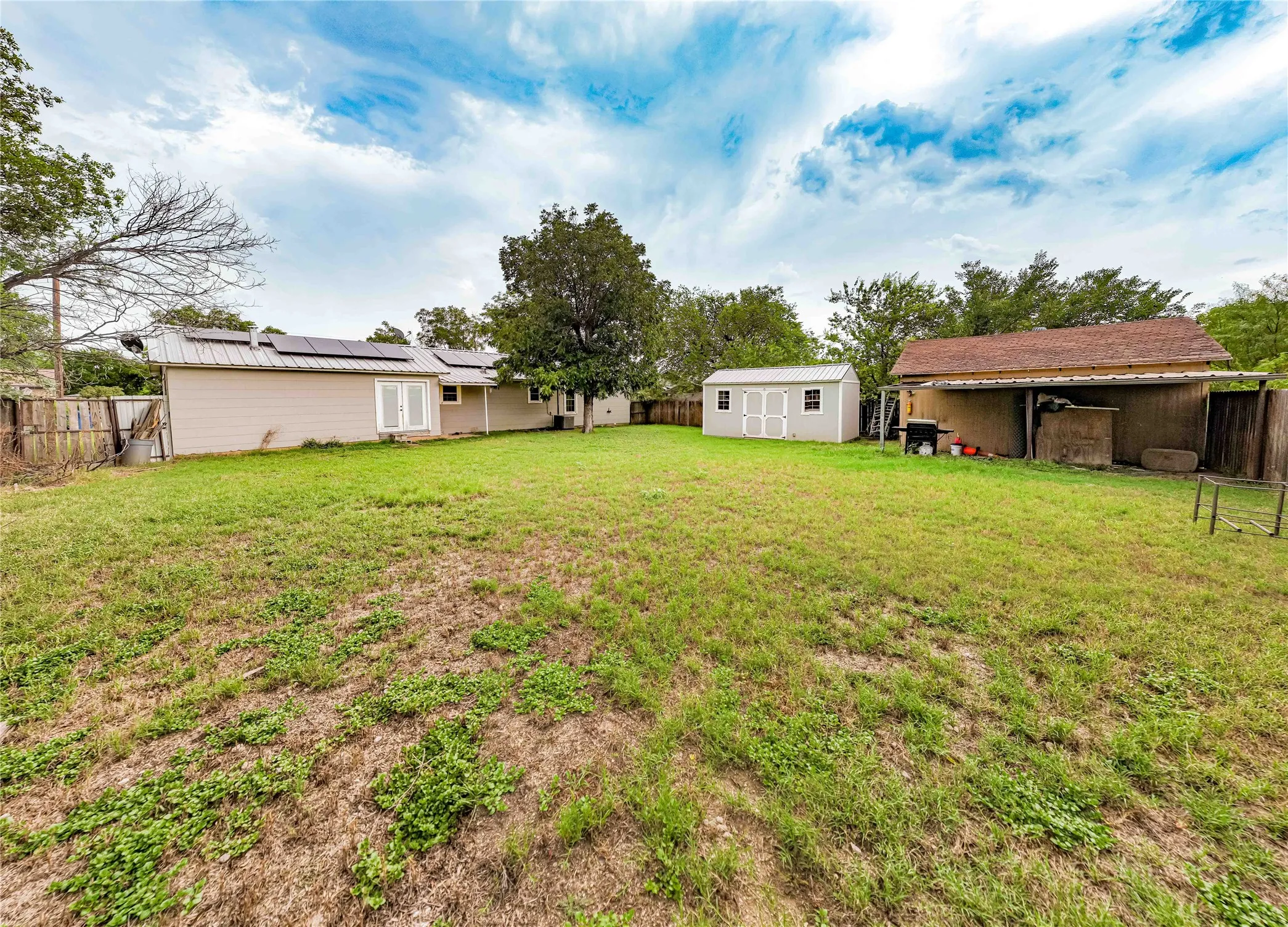Expansive backyard featuring a detached shed, a secondary utility structure with an overhang, and a wood privacy fence