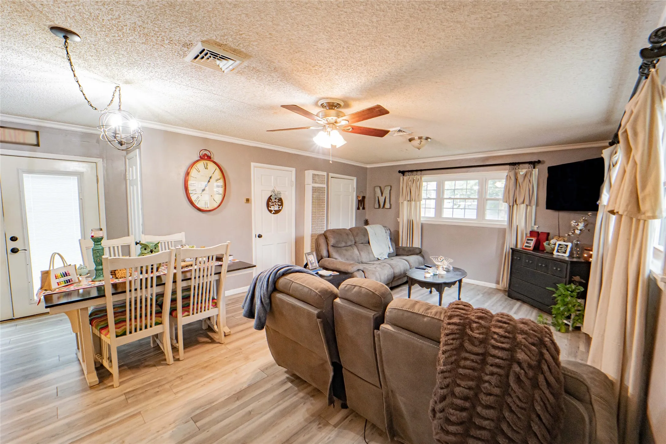 Open-concept living area featuring wood-finish flooring, a ceiling fan, and crown molding