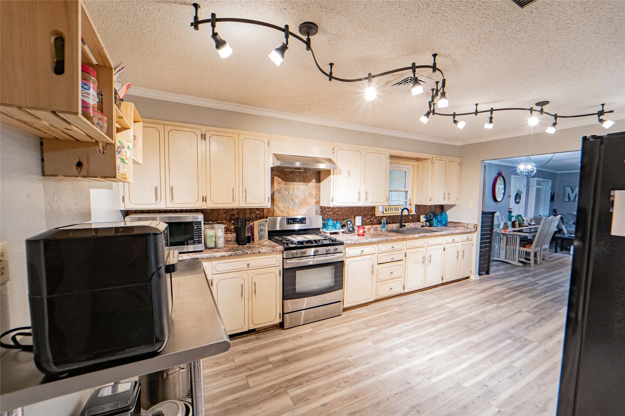 Kitchen featuring extensive cream cabinetry, track lighting, wood-finish flooring, a stainless steel range, and a copper-toned backsplash