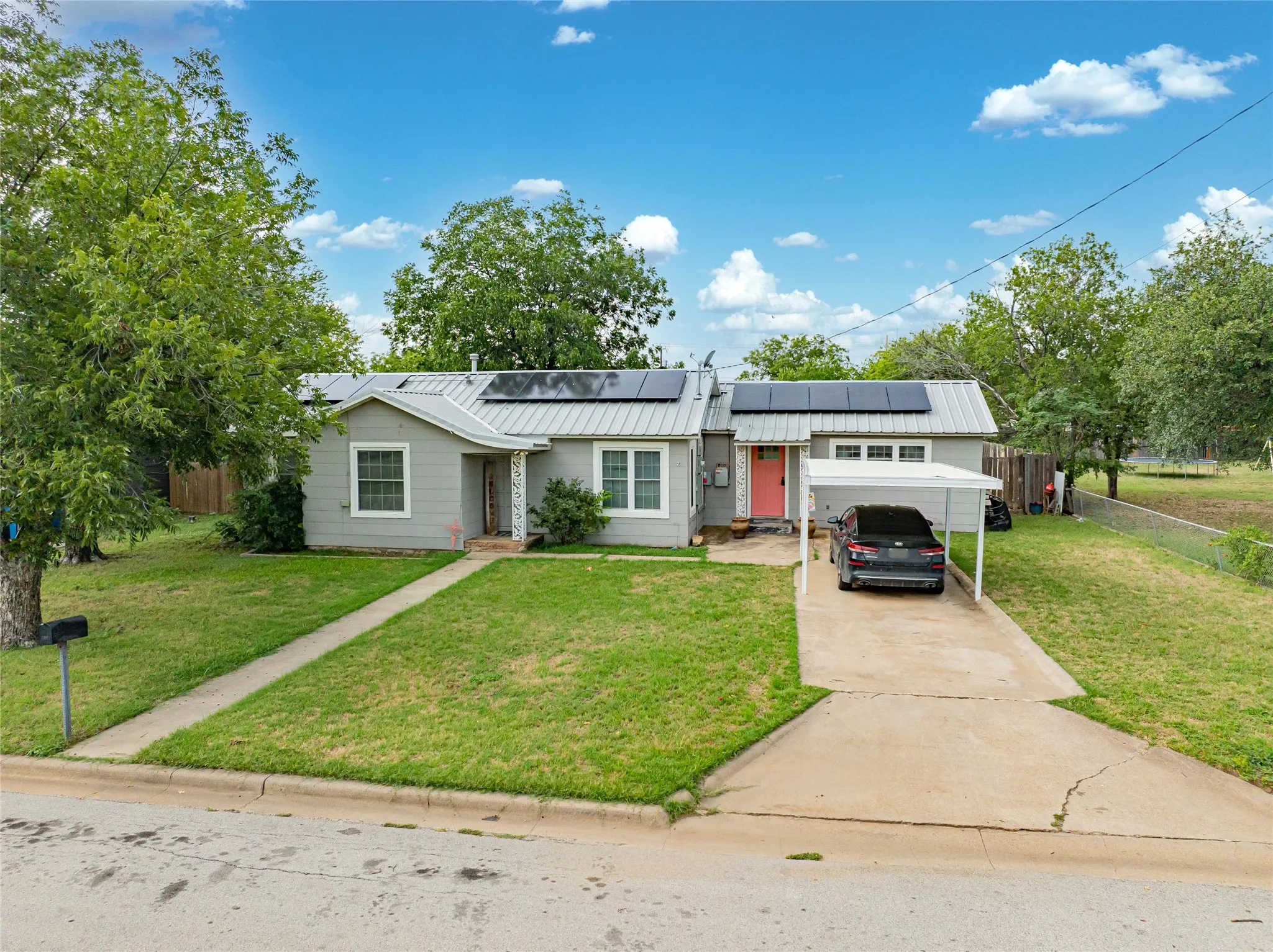 Ranch-style exterior with gray siding, multiple solar panels, a metal roof, and a vibrant orange-red entry door