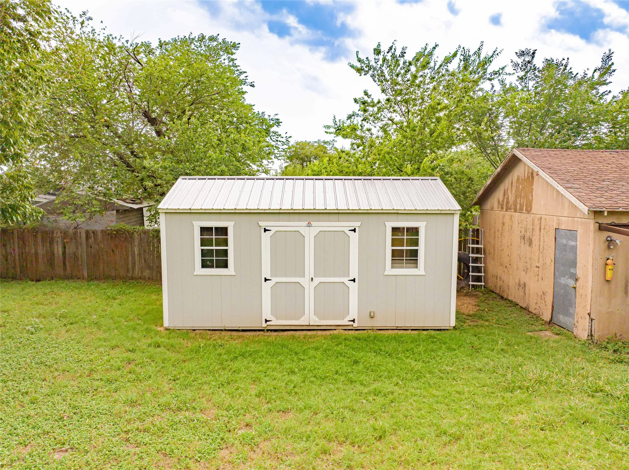 Detached storage shed featuring a metal roof, light-colored siding, and white trim