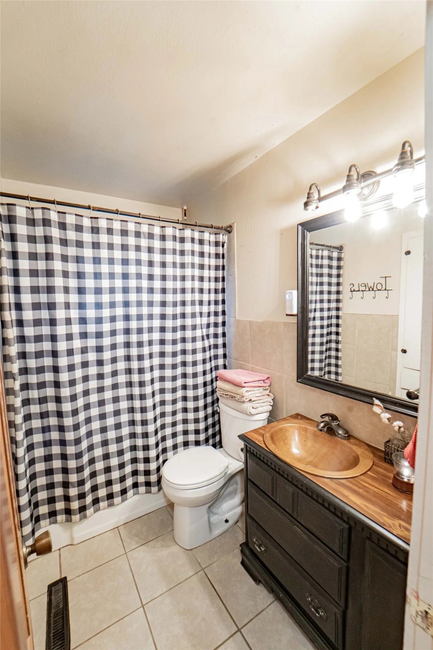 Bathroom featuring a wood-finish vanity with an integrated basin, a black framed mirror, a three-light vanity bar, and neutral floor tiling