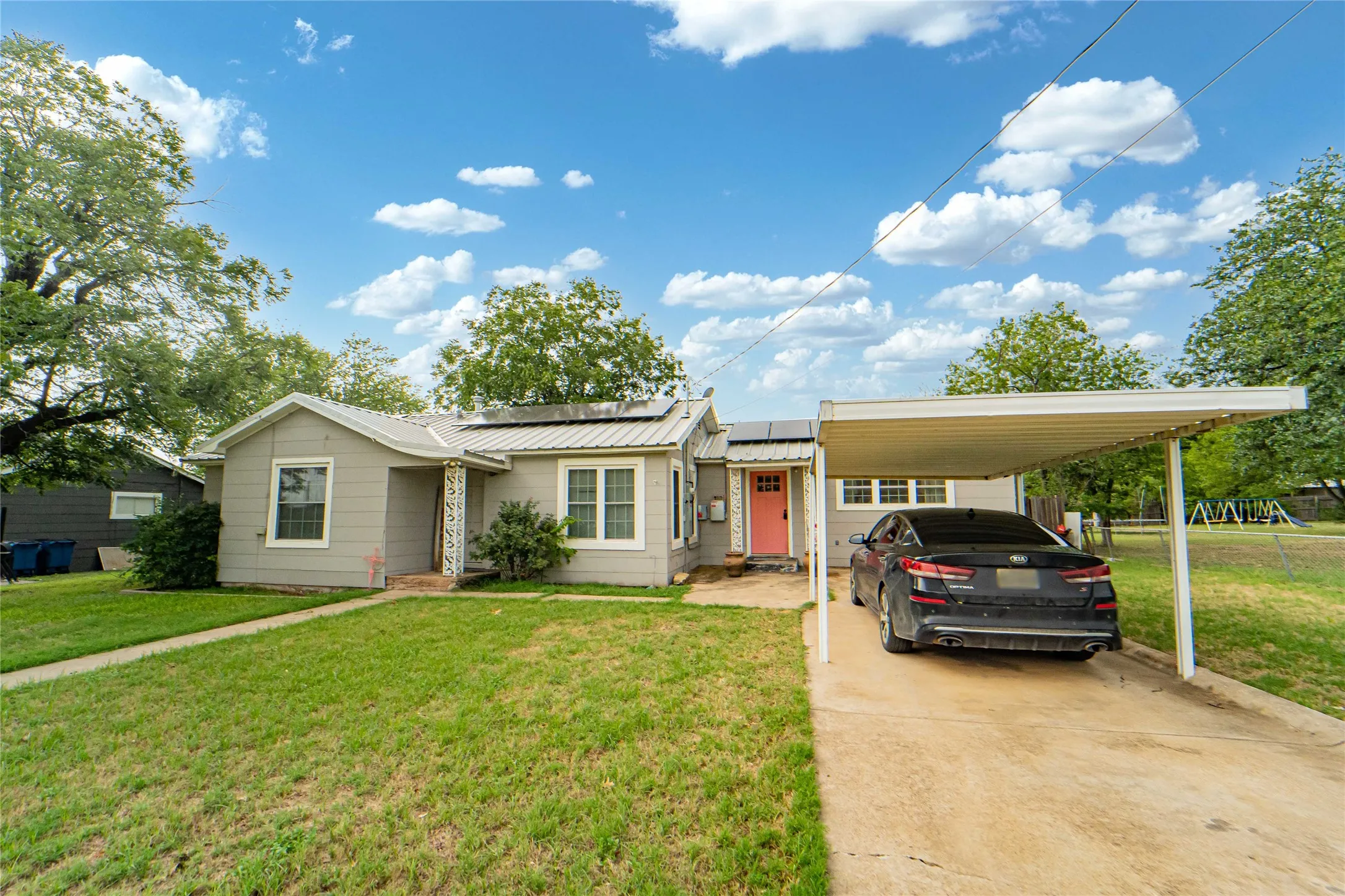 Single-story residence featuring a metal roof, front porch with decorative columns, and a bright coral entry door