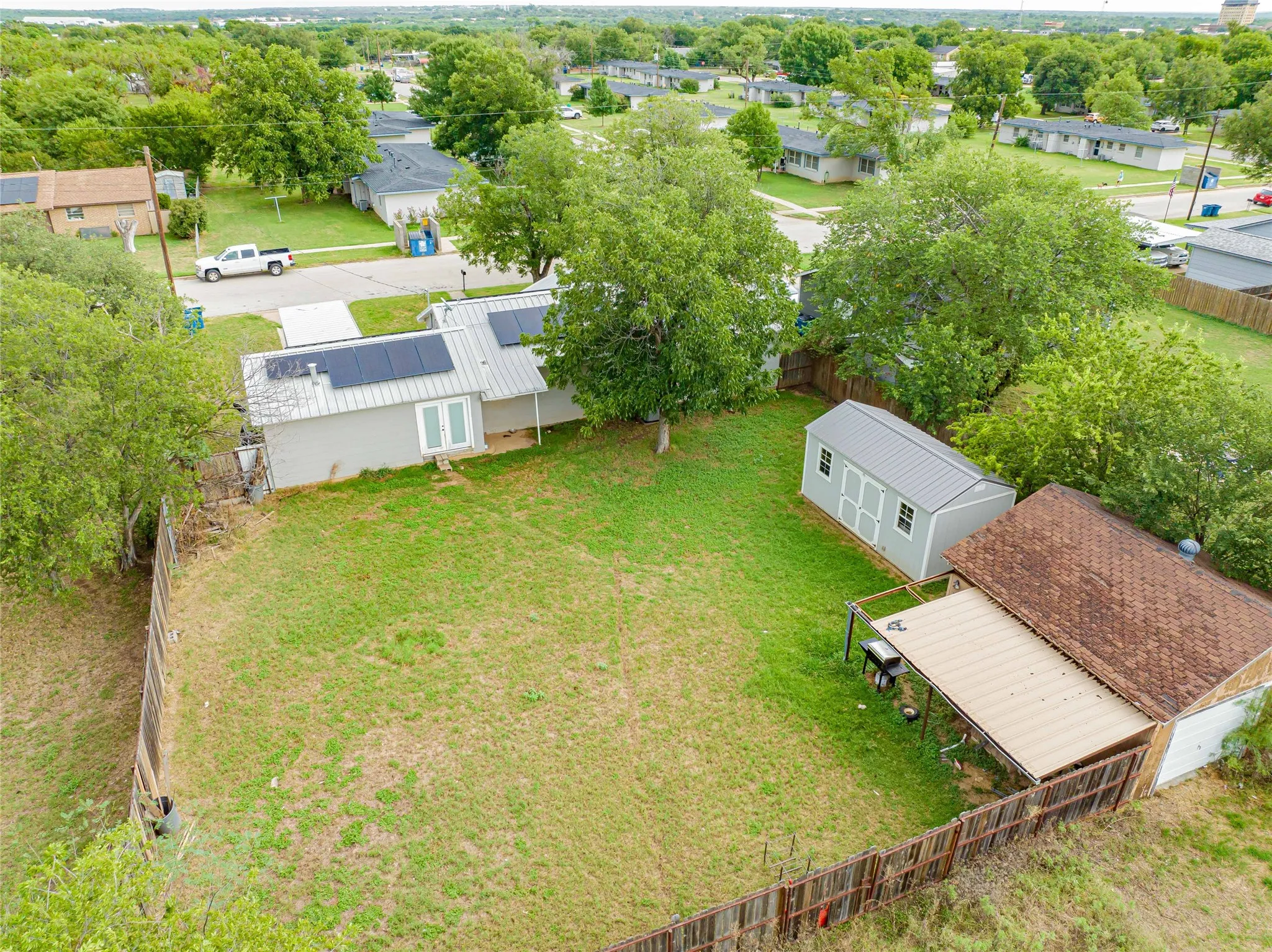 Expansive backyard featuring a wood fence, a detached shed with a metal roof, a covered patio area, and mature trees