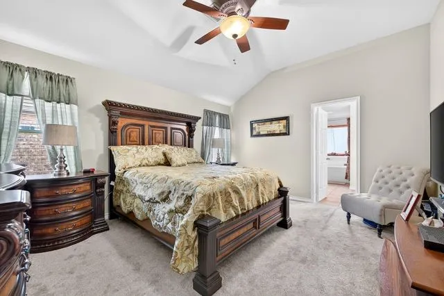 Carpeted bedroom featuring vaulted ceilings and a ceiling fan