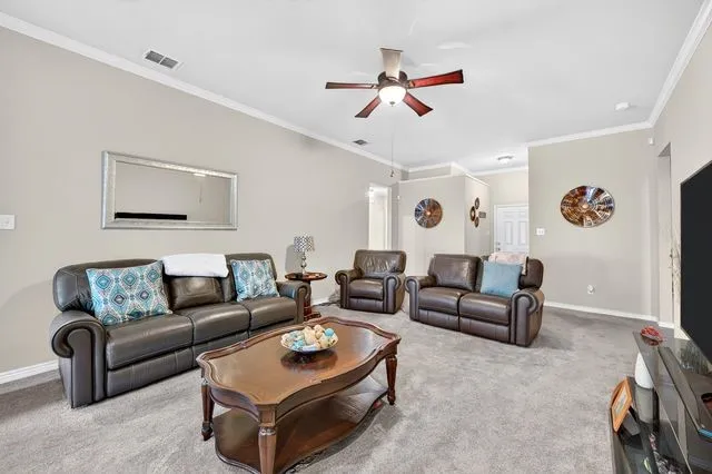 Spacious living area featuring neutral-toned walls, crown molding, and light gray carpeting