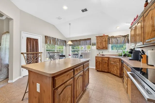 Kitchen featuring a center island with a light-colored countertop, wood cabinetry, stainless steel appliances, and a vaulted ceiling with recessed lighting