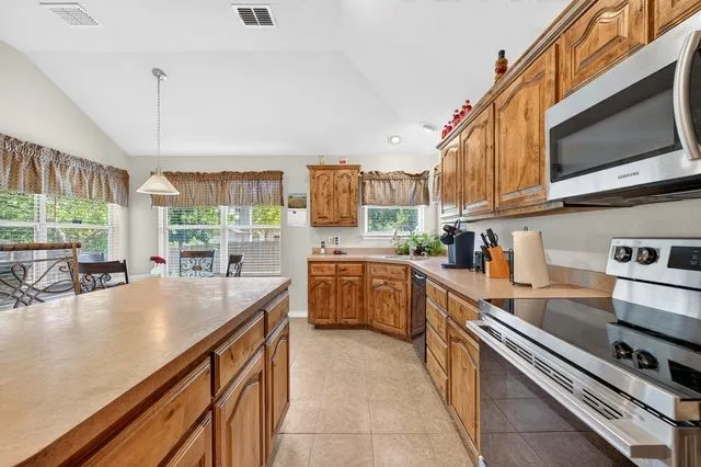 Kitchen featuring wood cabinetry, stainless steel appliances, a large central island with countertop, and tile flooring