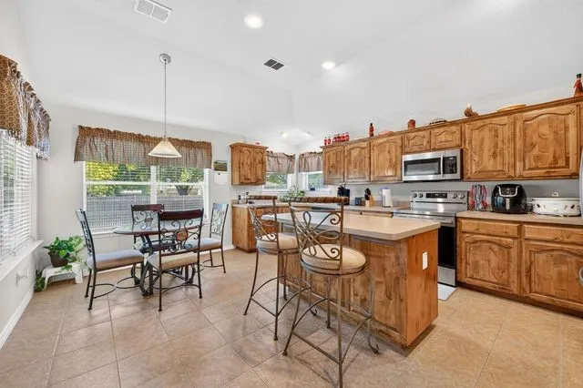 Expansive kitchen featuring wood cabinetry, stainless steel appliances, a center island with bar seating, and tile flooring