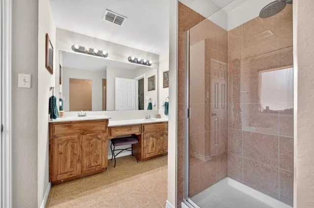 Dual vanity with light wood cabinetry, a large mirror, and tiled flooring