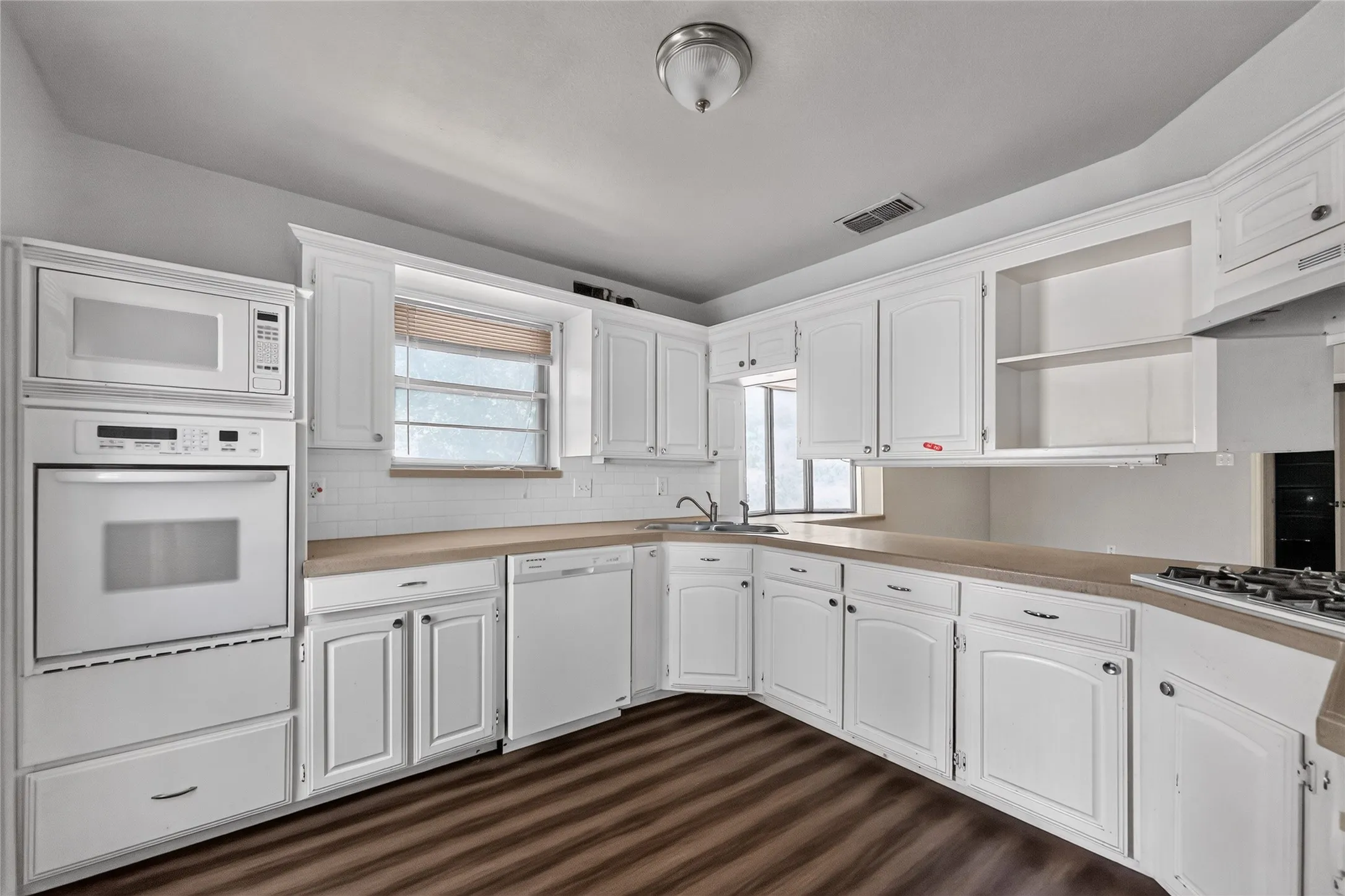 Kitchen featuring white cabinetry and built-in appliances, wood-finish flooring, a wall oven and microwave combination, a built-in dishwasher, and a gas cooktop