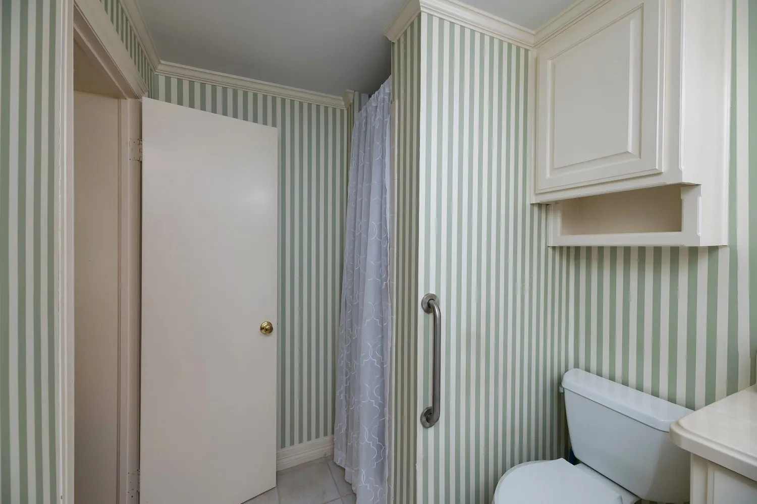 Bathroom featuring striped wallpaper, white upper cabinetry with an open shelf, a toilet, a shower curtain, and a wall-mounted grab bar