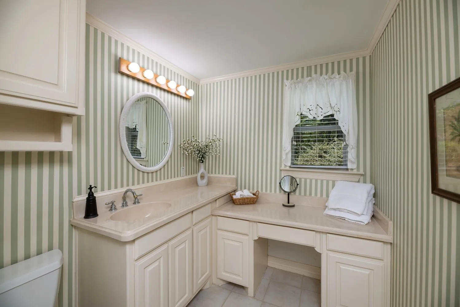Bathroom vanity featuring an integrated sink, built-in cabinetry, an oval mirror, and a dedicated vanity seating area