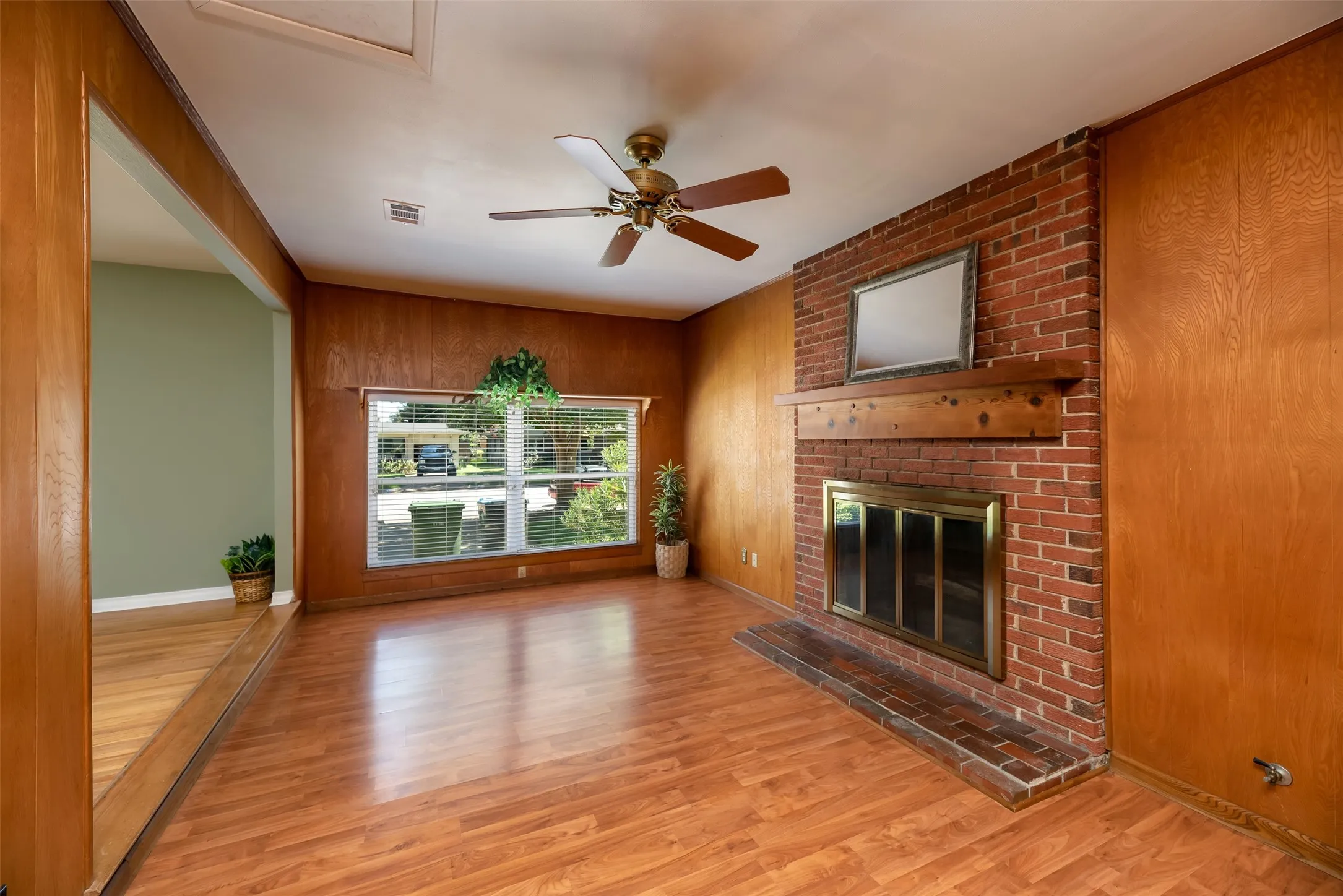 Living area featuring wood-finish flooring, a brick fireplace with a wood mantel, and wood paneling