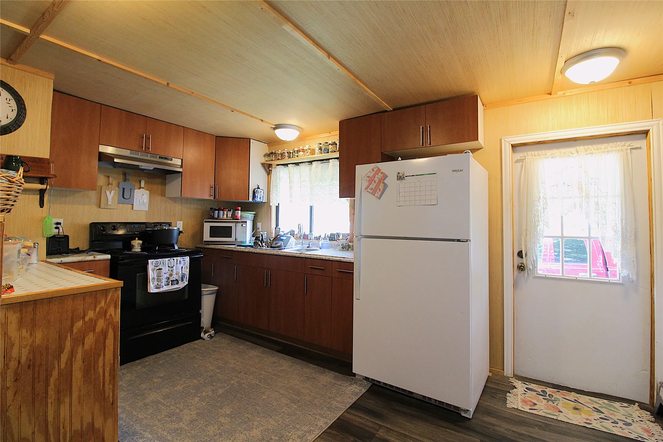 Kitchen featuring wood-finish cabinetry, black electric range with overhead vent, and a white refrigerator