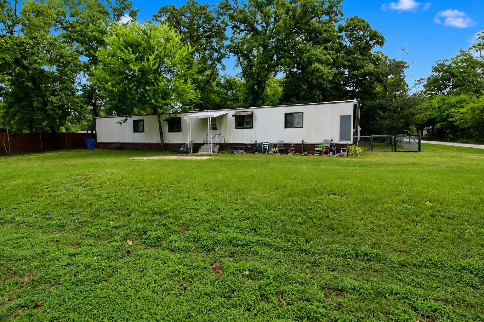 Expansive green lawn surrounds the property, featuring a white mobile home with dark trim windows and a covered entry porch
