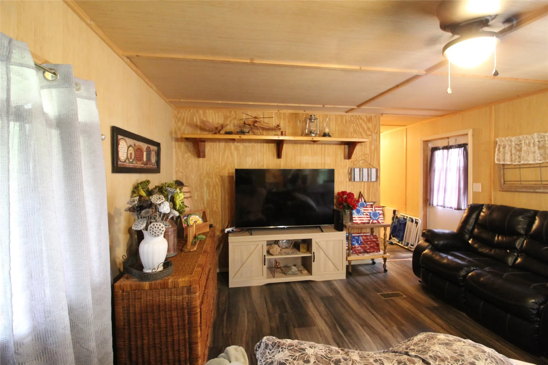 Living area featuring wood-finish laminate flooring, panel walls, and a ceiling fan with integrated lighting