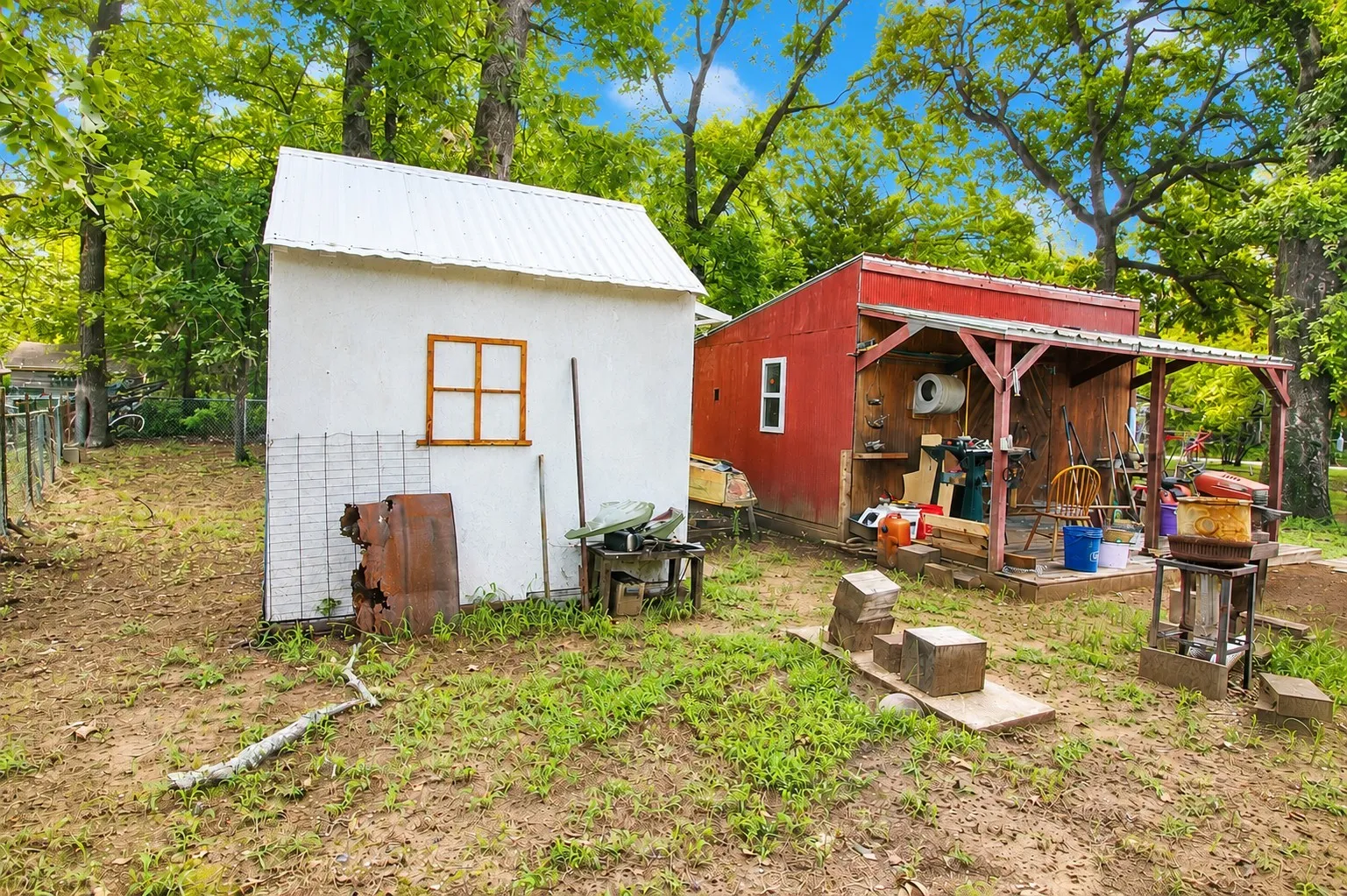Two outbuildings featuring a white shed with a window and a red shed with an open-air covered porch area