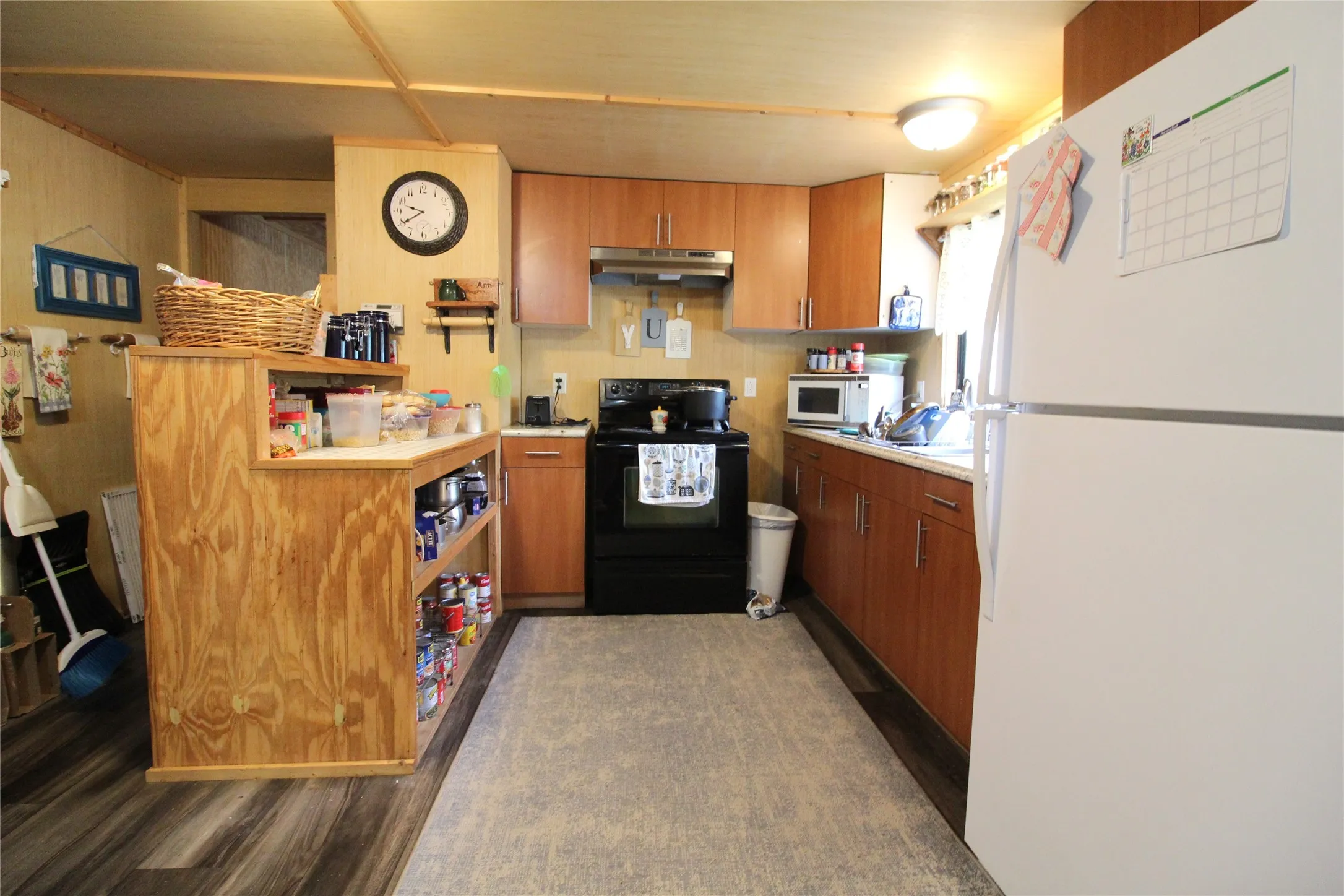Kitchen featuring wood-finish flooring, wood cabinetry with brushed nickel hardware, light-toned countertops, and a full-size white refrigerator