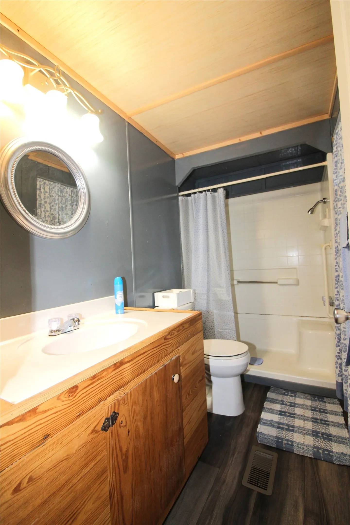 Bathroom featuring a wood-finish vanity with an integrated sink, a circular framed mirror, wood-finish flooring, a shower-tub combination, and a wood-panel ceiling