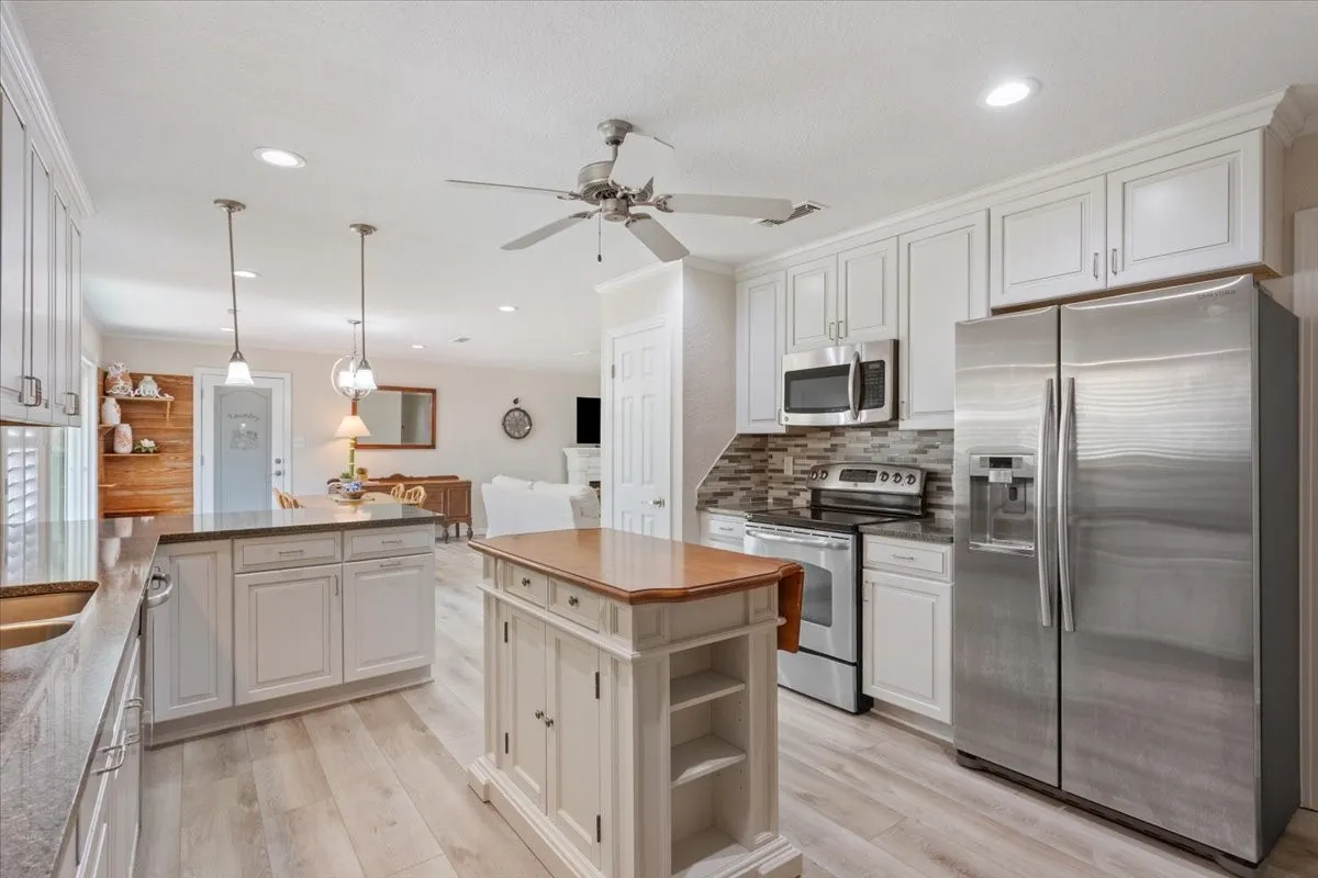 Kitchen featuring white cabinetry, stainless steel appliances, a multi-tone tile backsplash, and light wood-finish flooring