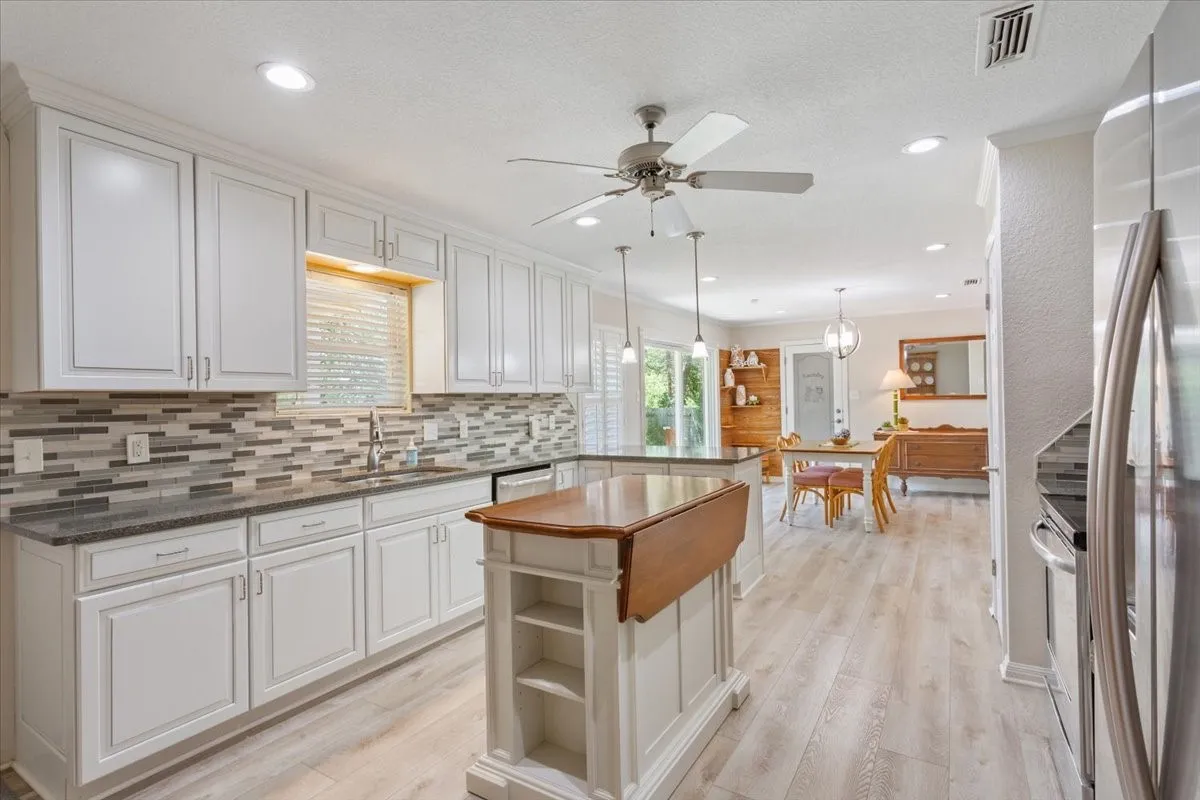 White cabinetry, stone countertops, mosaic tile backsplash, wood-finish flooring, and recessed lighting