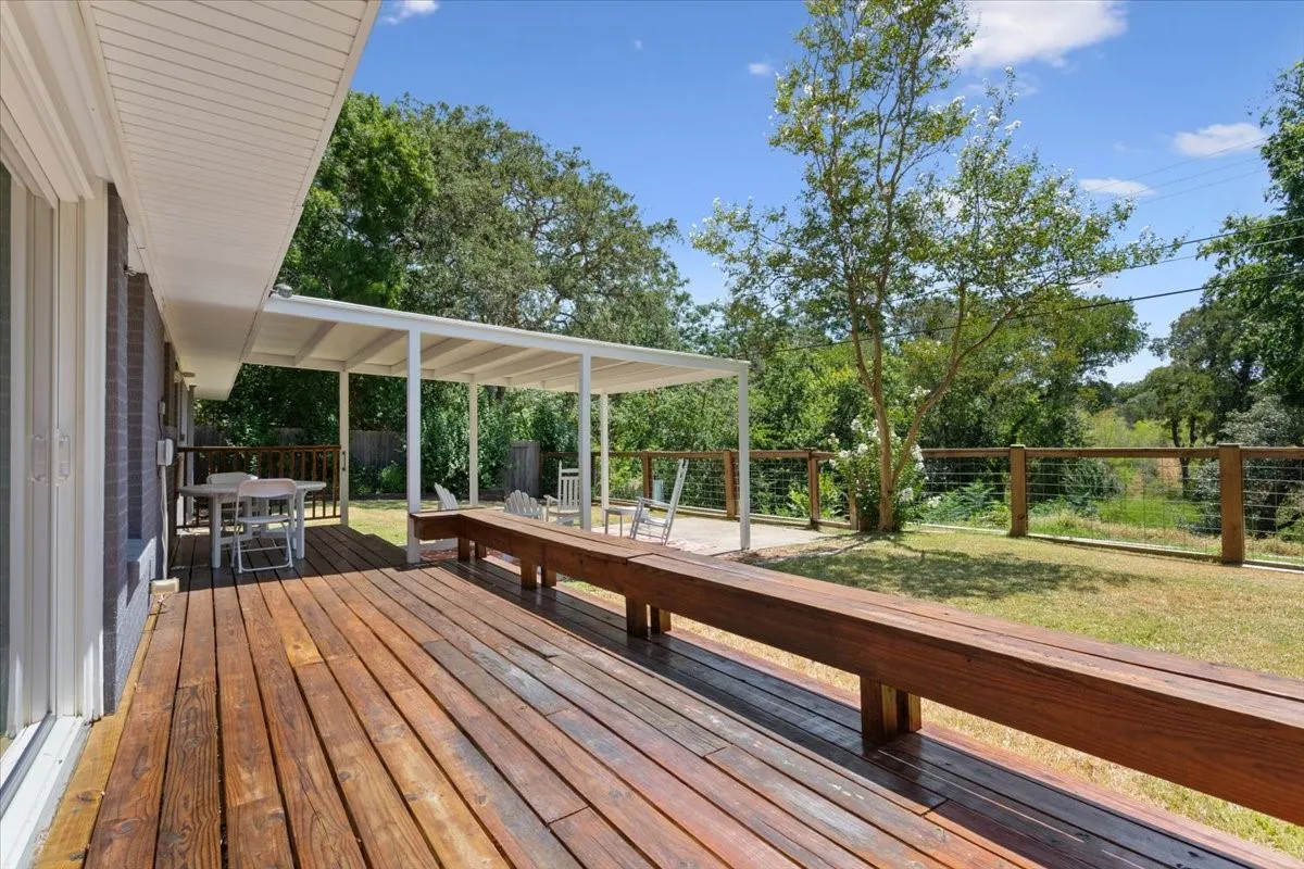 Expansive wood-finish deck with built-in seating, a covered patio area, and a white metal pergola